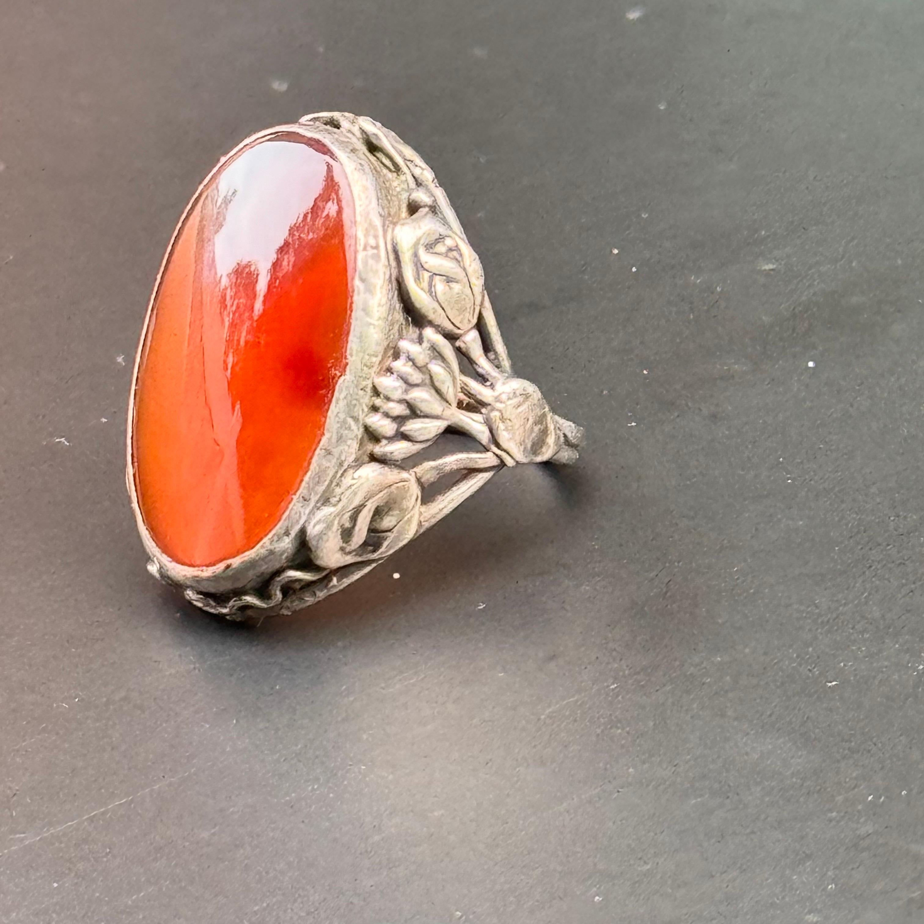 Découvrez le charme exquis de cette bague vintage, réalisée de main de maître dans les styles Arts & Crafts et Art Nouveau. Cette pièce présente des motifs floraux complexes et une pierre naturelle étonnante. Le centre est orné d'un grand cabochon