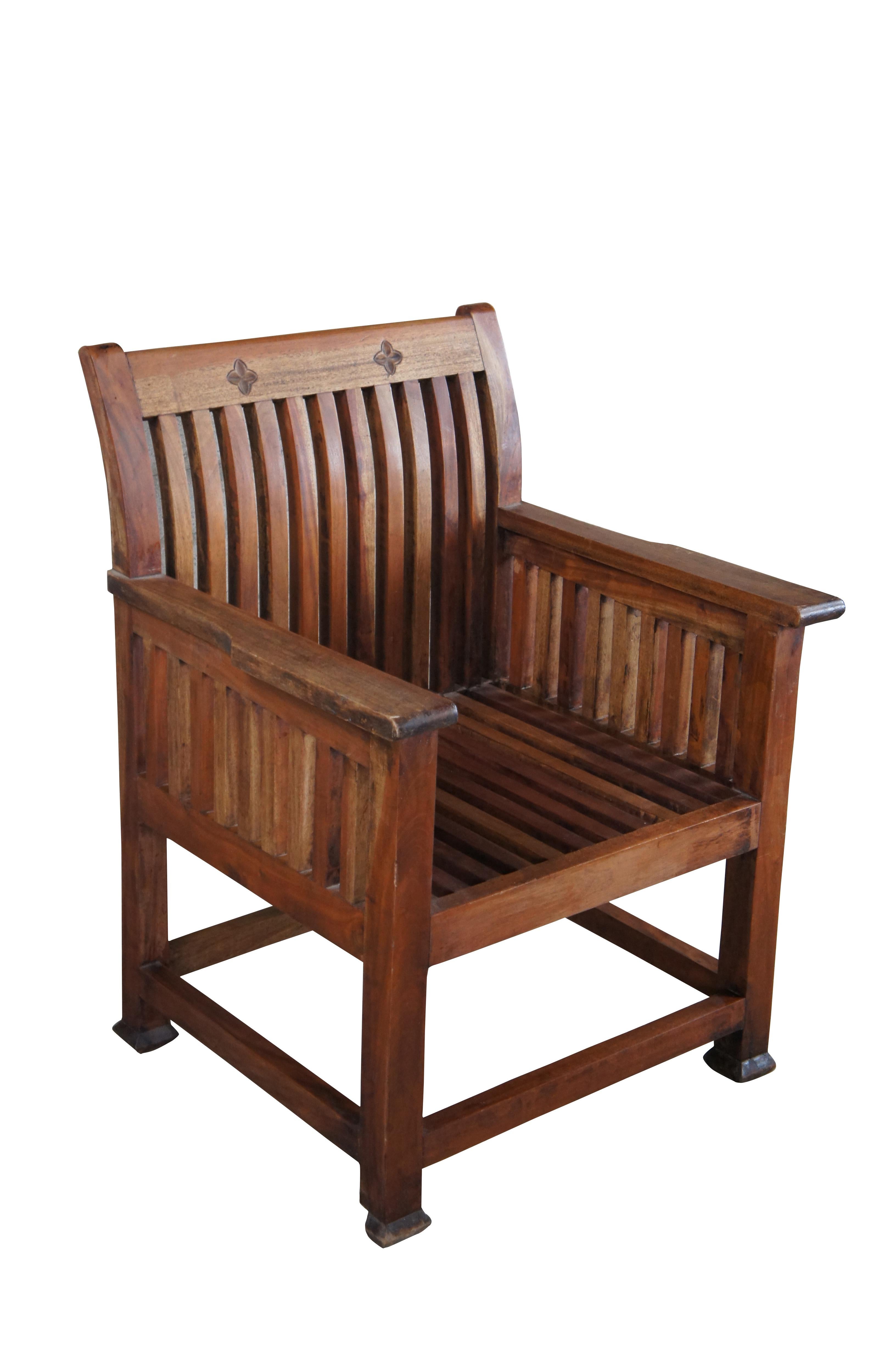 Solid teak arm chair. Features a square form with slatted back and sides. Back is flared with two carved florets. 

Dimensions:
26