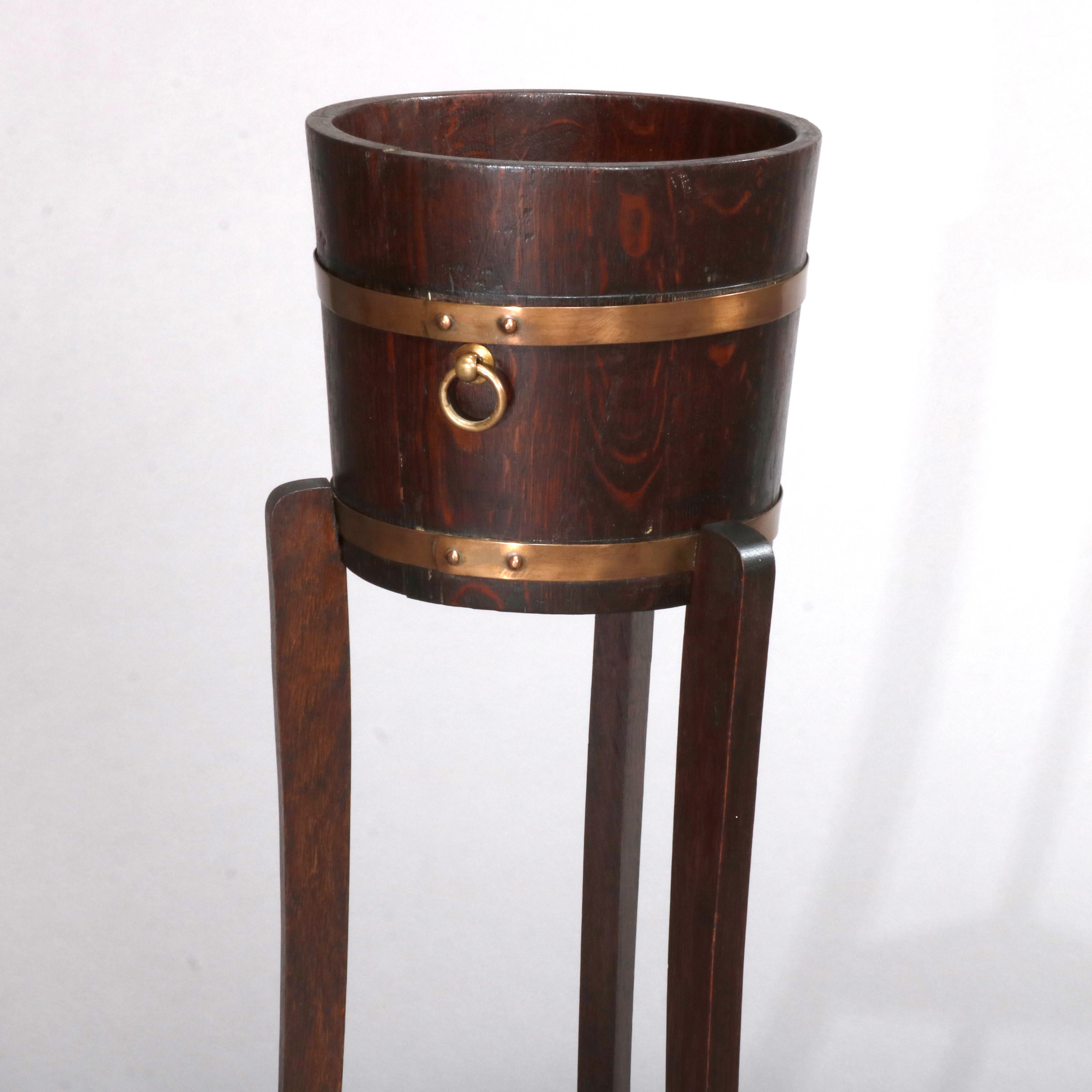 A vintage Arts & Crafts planter with stand in the manner of Stickley offers oak construction with banded bucket form jardinière seated on convex tripod stand having lower triangular shelf, circa 1930

Measures: 35.75