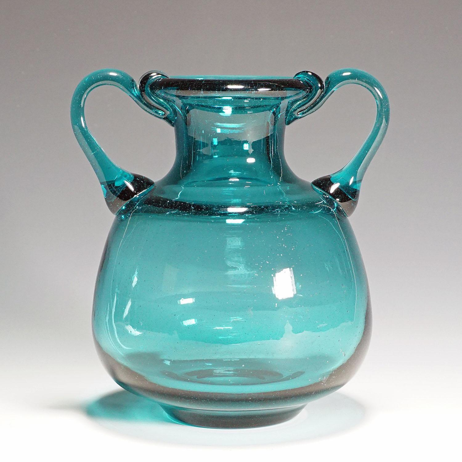 A nice glass vase with two handles. Manufactured in massive petrol colored glass with fine air bubbles inside. Manufactured by the Ichendorfer Glassworks, Germany around 1960. The Ichendorfer glass works issued a series of replicas of antique roman