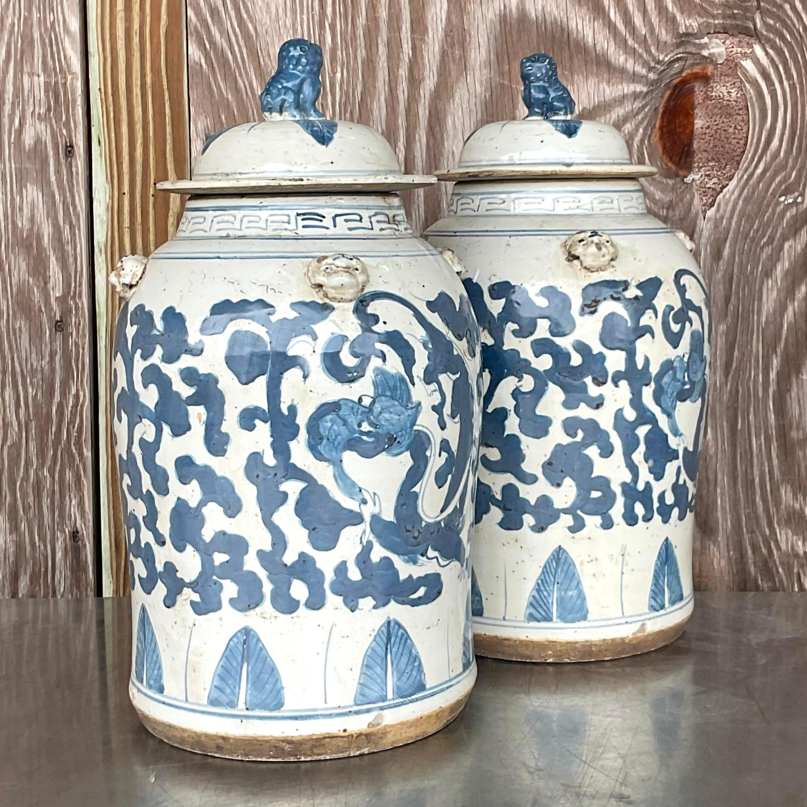 Une superbe paire d'urnes asiatiques vintage. Un motif emblématique bleu et blanc peint à la main. Chaque urne est surmontée d'une belle paire de chiens de chasse. Acquis d'une succession de Palm Beach