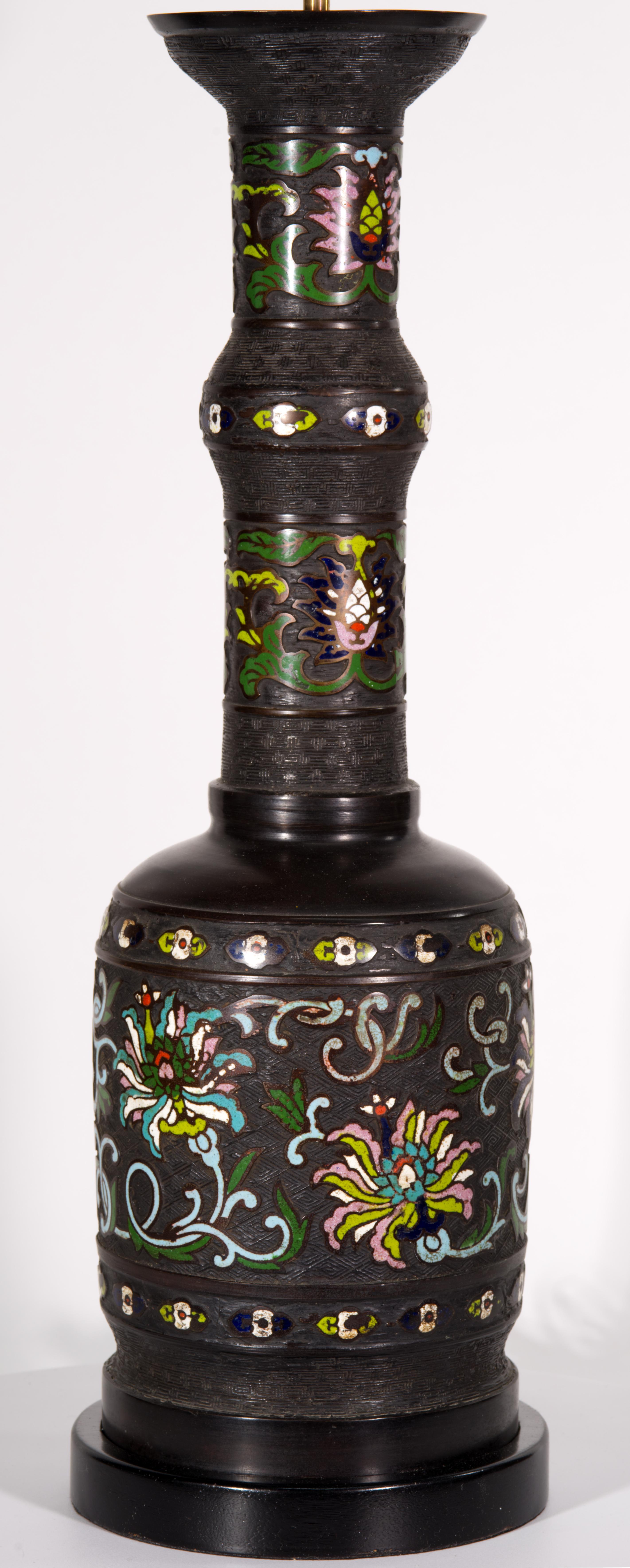  Extra-large vintage table lamp features sculptural urn shaped bronze body with elongated graphic neck that gives it a baluster silhouette. The lamp is decorated with enameled cloisonné designs, forming wide bands of white, green, and pink flowers
