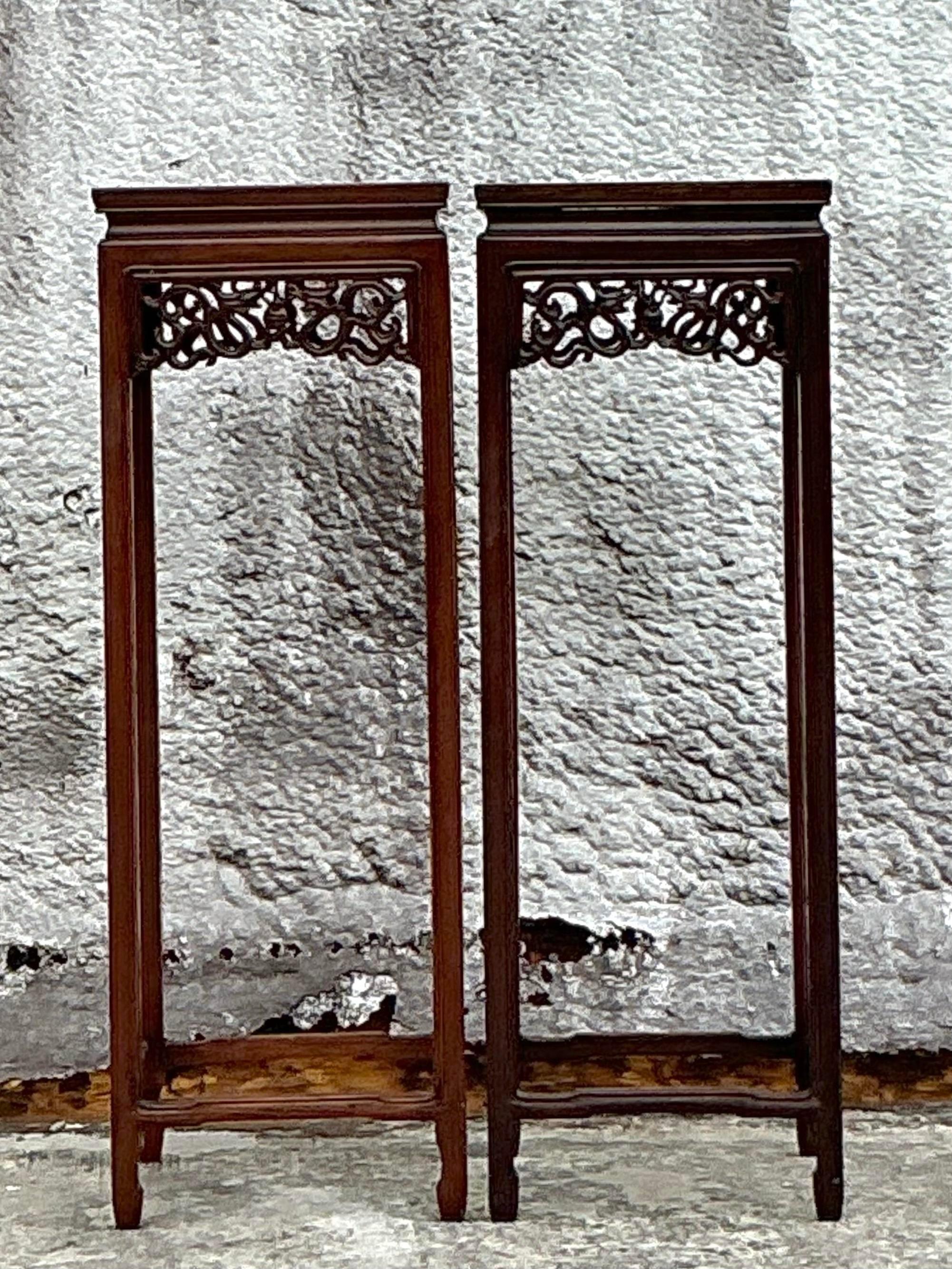 Elegante paire de piédestaux vintage en bois de rose asiatique, sculptés de façon experte avec des motifs floraux et géométriques complexes. Ces piédestaux mettent en valeur les tons riches et profonds et le grain magnifique du bois de rose, offrant