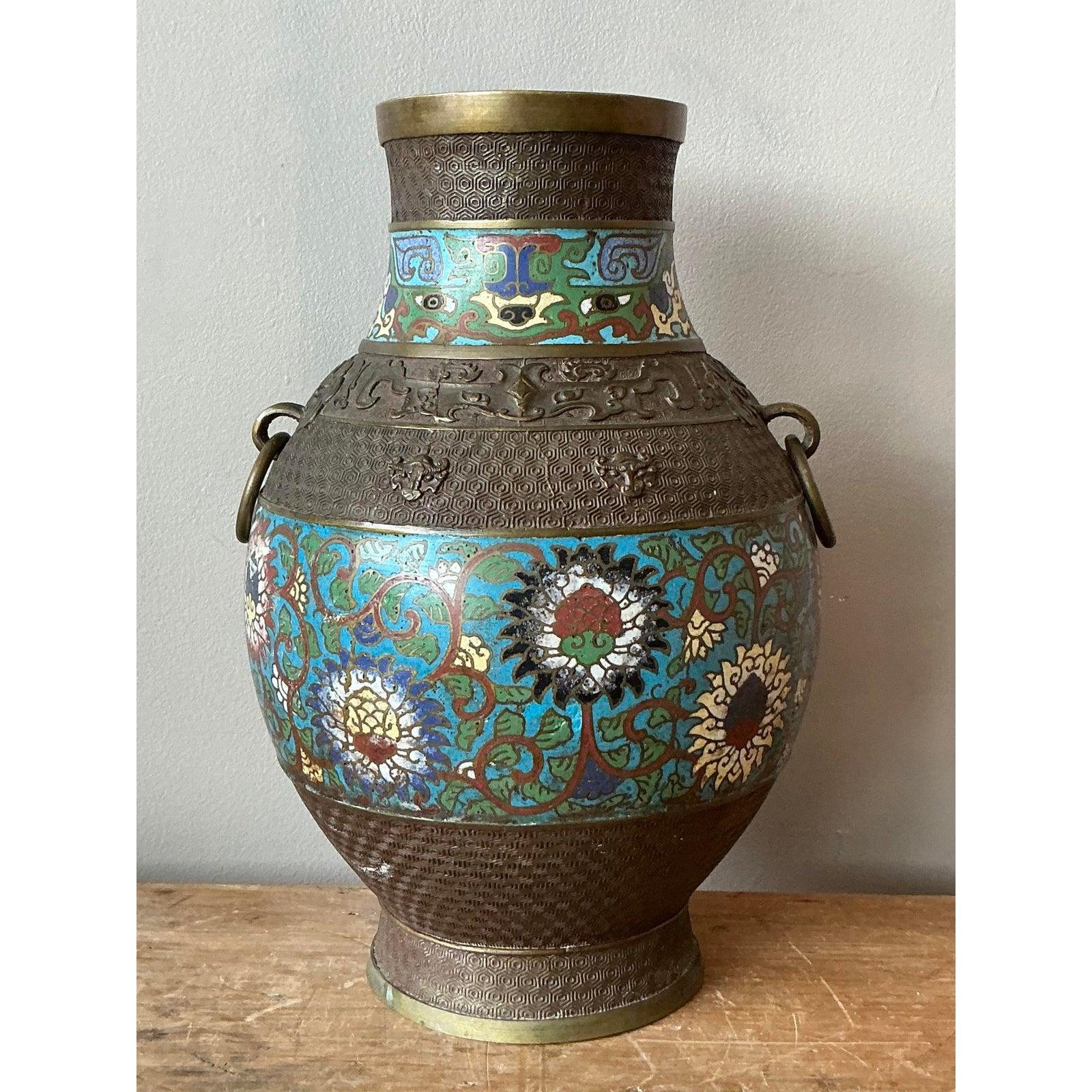 Questo magnifico vaso cloisonné vintage è un superbo esempio di arte decorativa tradizionale asiatica, che si distingue per la vibrante smaltatura e l'intricata lavorazione del metallo. Il corpo robusto a forma di balaustro è realizzato in bronzo e