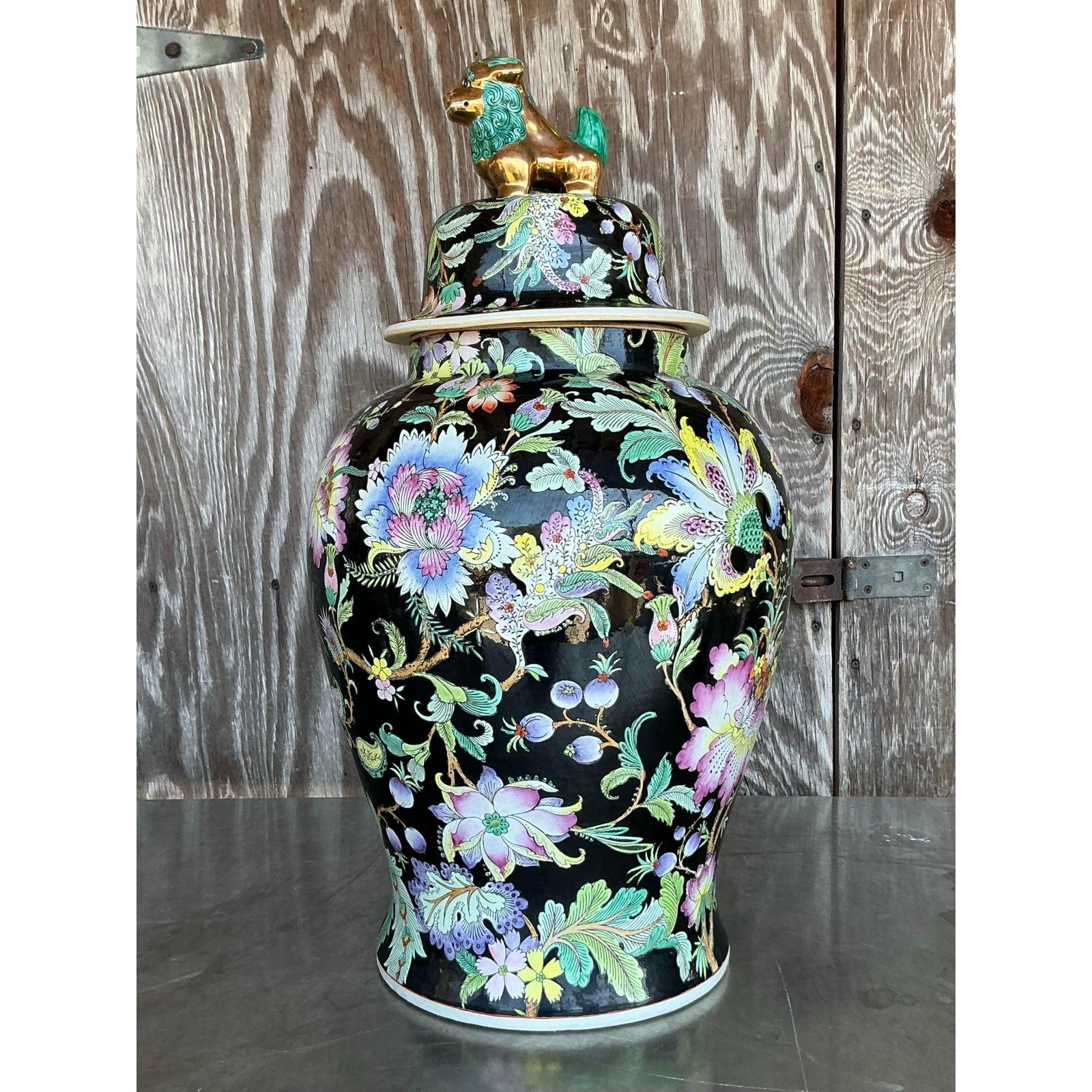 Infuse your space with vibrant heritage and timeless artistry with this vintage Asian floral ginger jar. This lidded porcelain vessel dazzles with a rich black ground adorned in radiant pastel florals, all intricately hand-painted with gold-accented