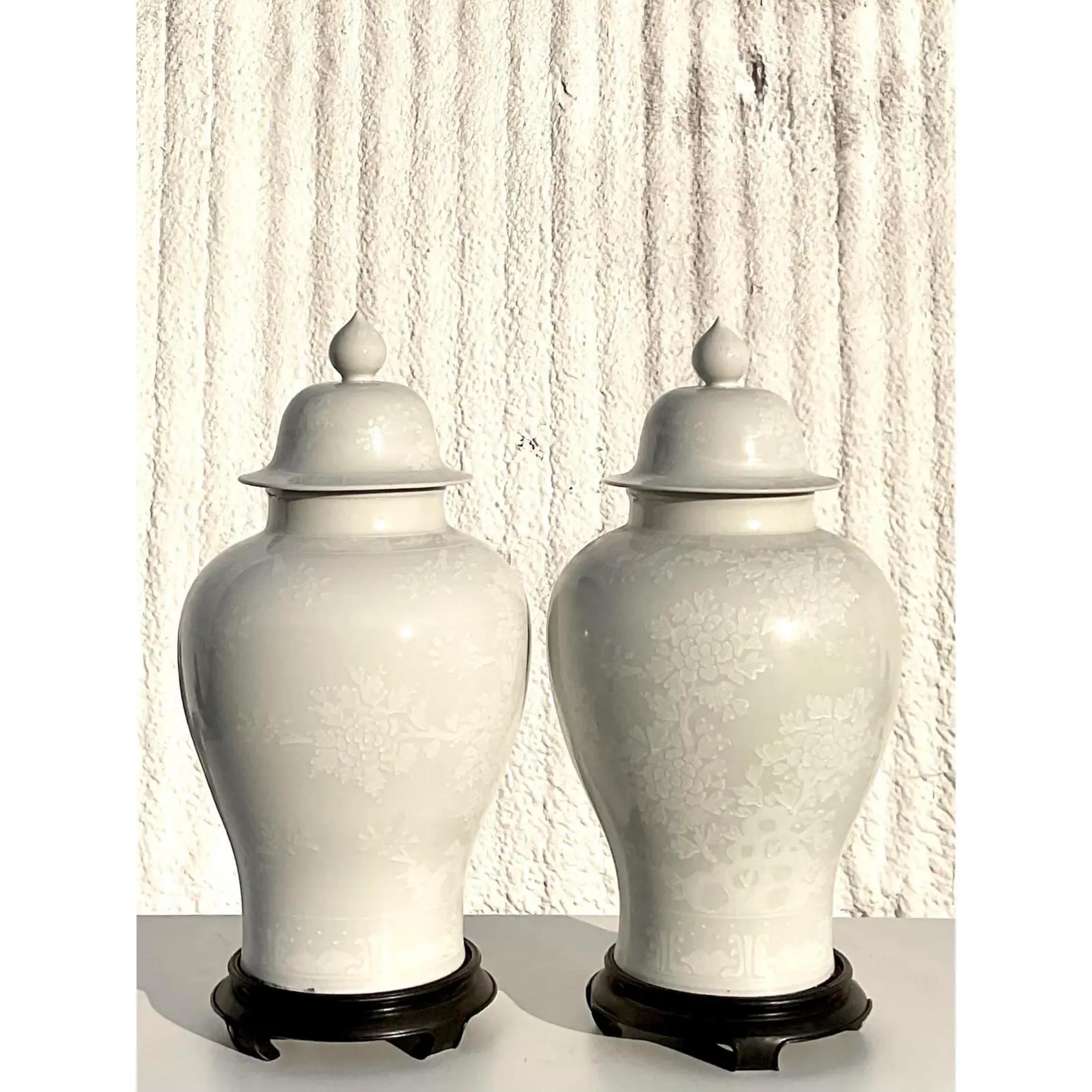 Fabulous pair of white Asian ginger jar urns. Beautiful tone on tone floral design. Rest on ebony wooden plinths. Acquired from a Palm Beach estate