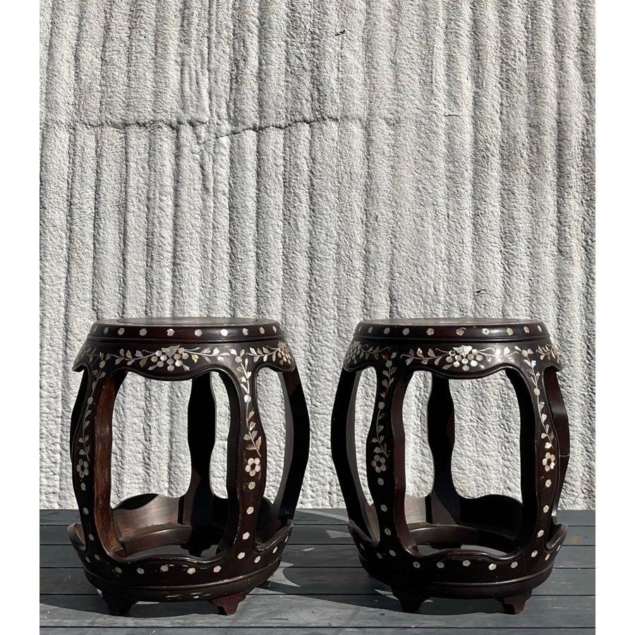 a splendida coppia di sgabelli asiatici vintage è una vera e propria celebrazione dell'artigianato e dell'arte. Ogni sgabello presenta una splendida struttura in legno massiccio intagliato e impreziosito da intarsi in madreperla, con motivi floreali
