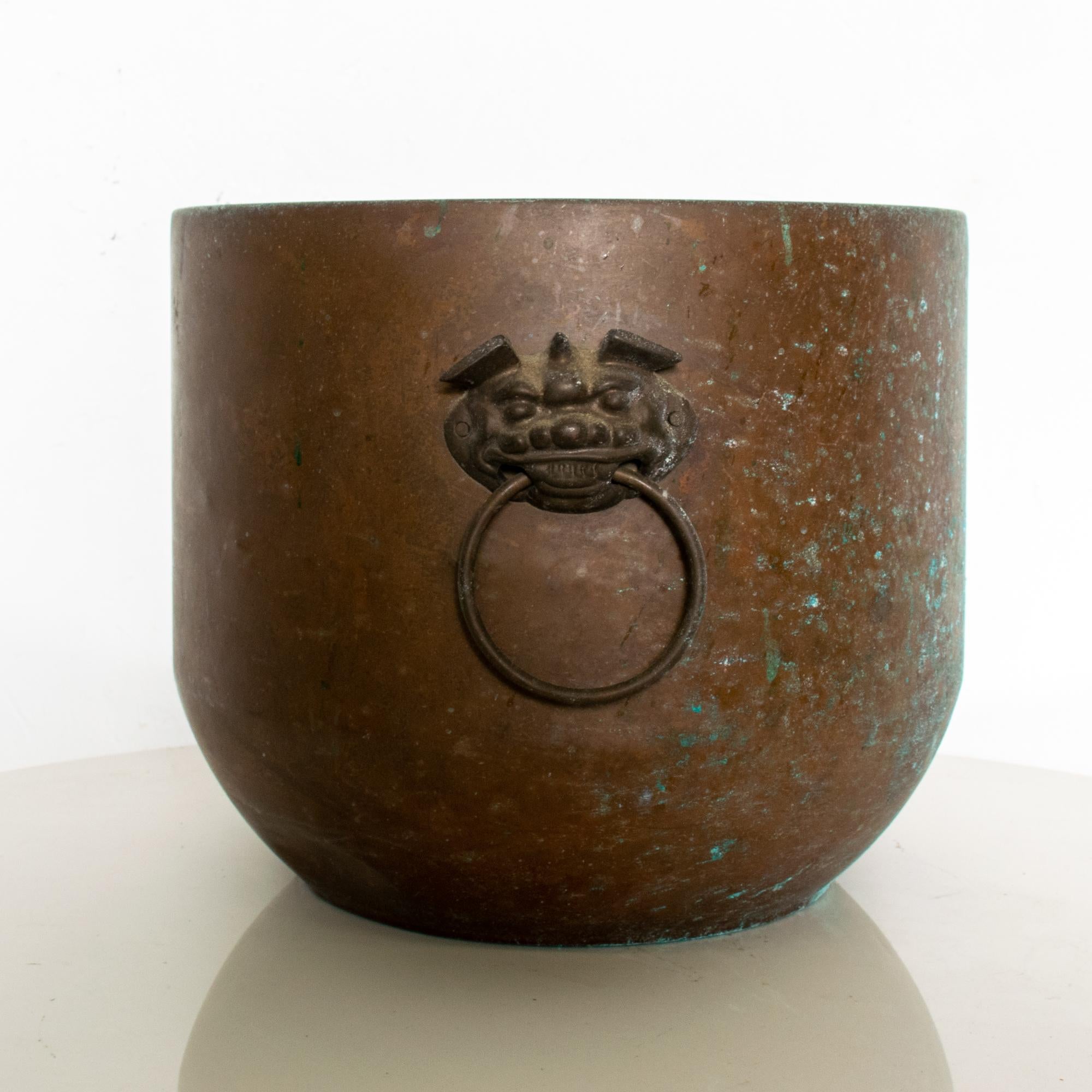 Hollywood Regency Asian jardinière planter pot in patinated brass.
Round shape with two side handles. The ring handles are attached to the planter by two protective Foo dogs in brass. Measures: 8 1/2