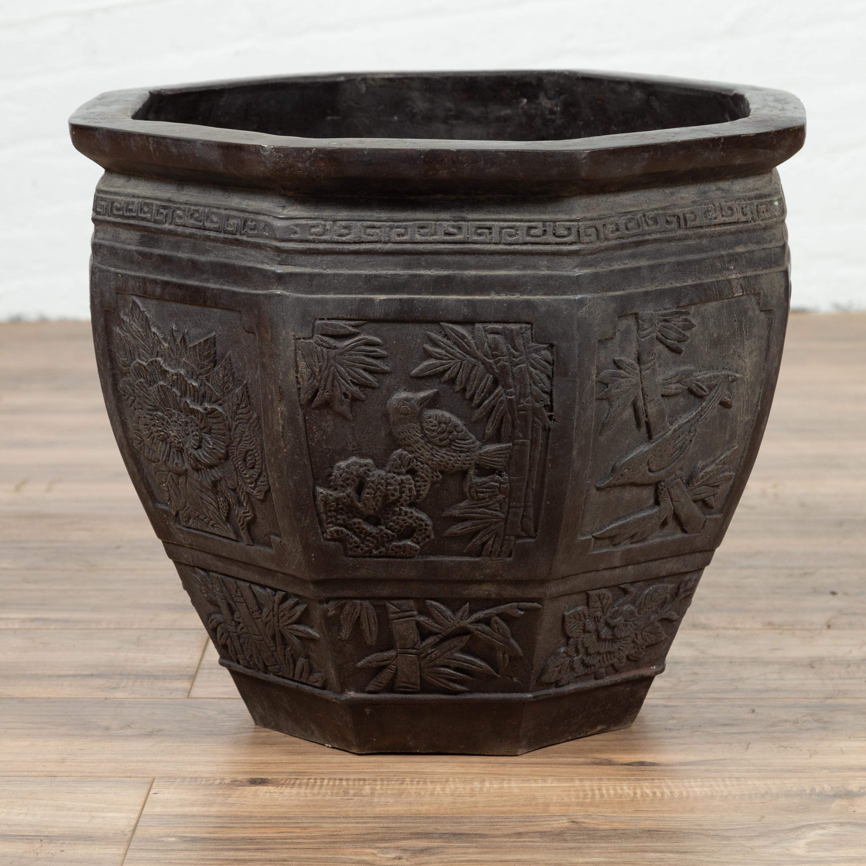 An Asian vintage bronze planter with floral and bird motifs. Presenting an octagonal shape and a dark patina, this handsome bronze planter features a beveled lip sitting above a tapering body, adorned in its upper section with a classical Meander.