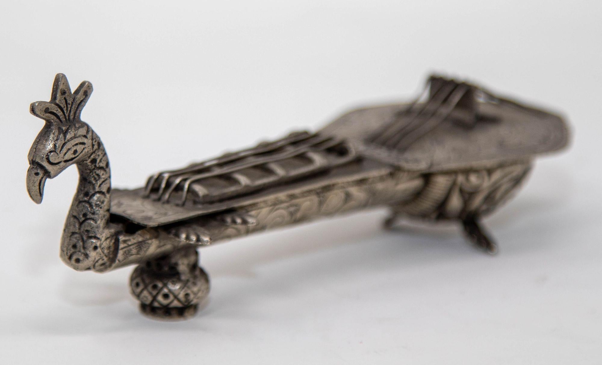 Vintage Asian Silver Metal Hand-Carved Sitar Veena Box.
Rehaussez votre décor avec cette superbe boîte vintage, ornée de motifs complexes d'un sitar et d'un paon, sculptés à la main. Le couvercle à charnière orné présente un motif d'oiseau