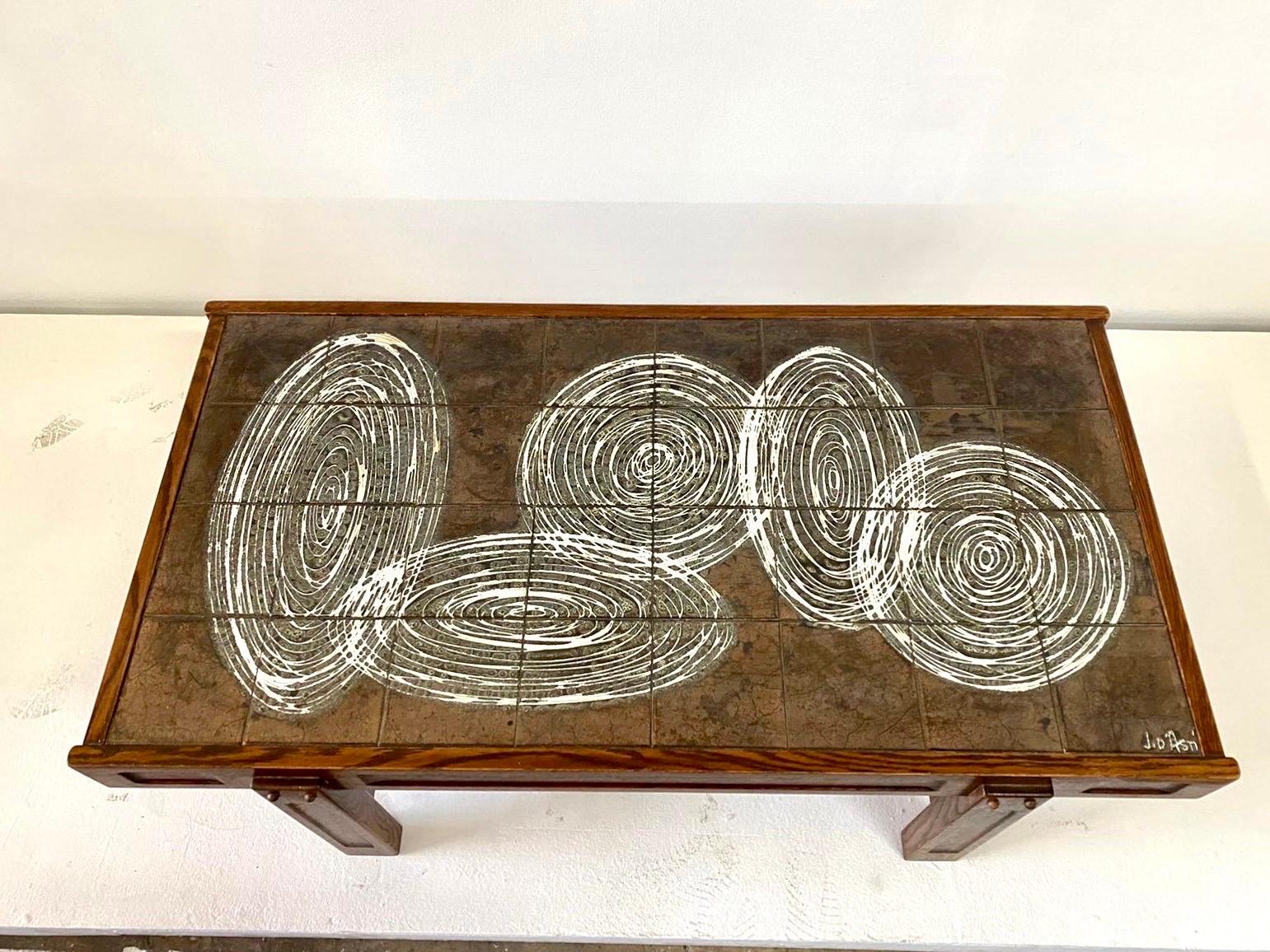 This wonderfully modern yet vintage ceramic top tiled coffee table, made in Vallauris, France circa 1960's. The design and colors are very relevant today, white intertwining circles and ovals to dark iridescent background and natural wood frame.
