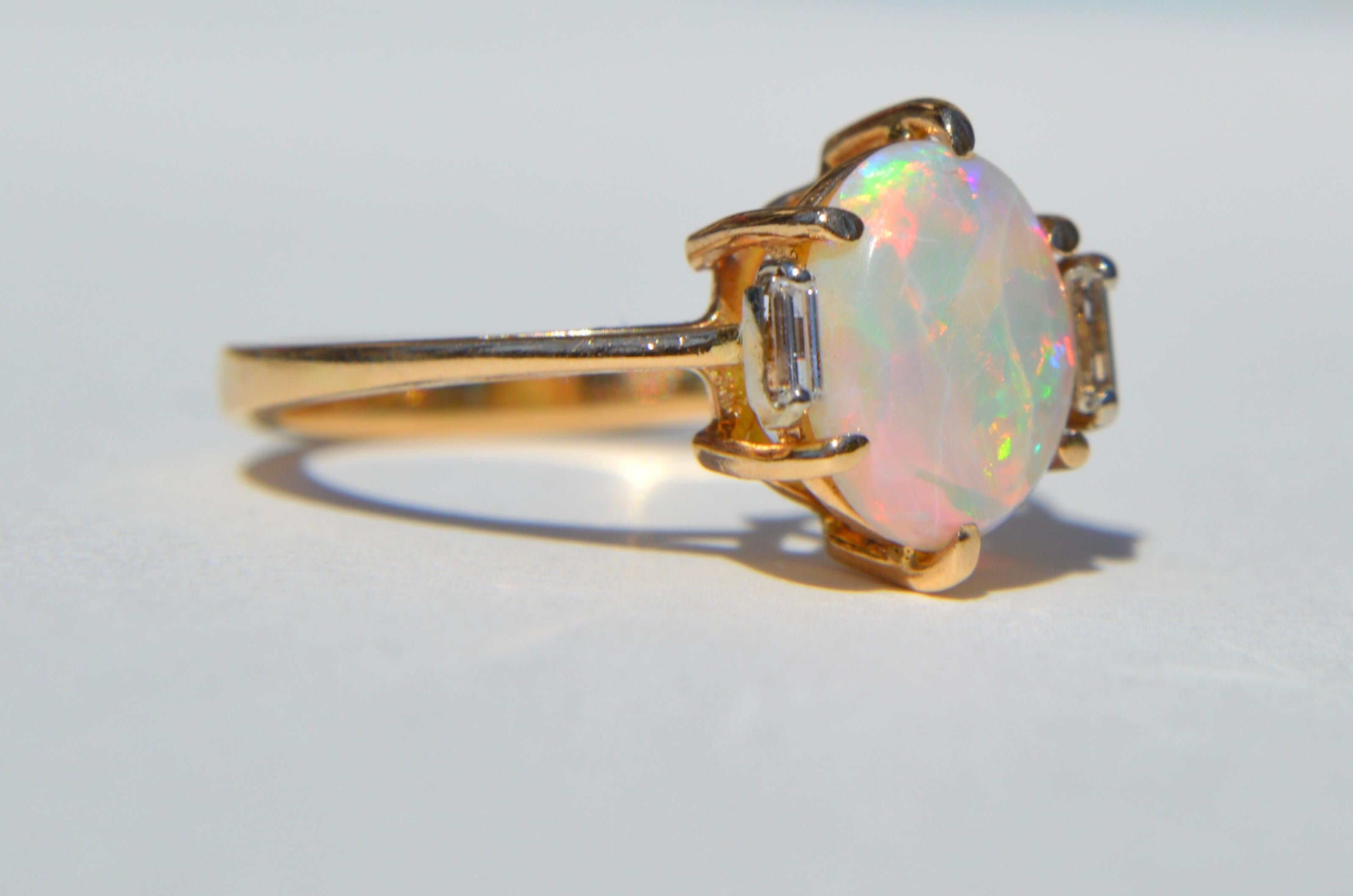 Gorgeous vintage circa 1970s Australian fiery rainbow flecked opal oval 3.85 carat cabochon (11x9mm) with two  baguette diamonds, each .1 carat has (3x1.5mm) set in solid 14K yellow gold. Size 7.5, can be resized by a jeweler. In very good