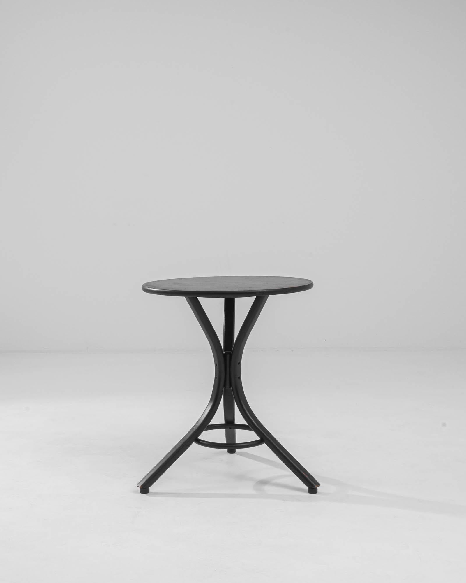 A pair of bentwood tables made in 20th century Austria, in the style of Thonet. A tripod of slender curving legs meet at the table’s center and taper outwards, supported by a thin circular stretcher. The black paint that covers the table’s surface