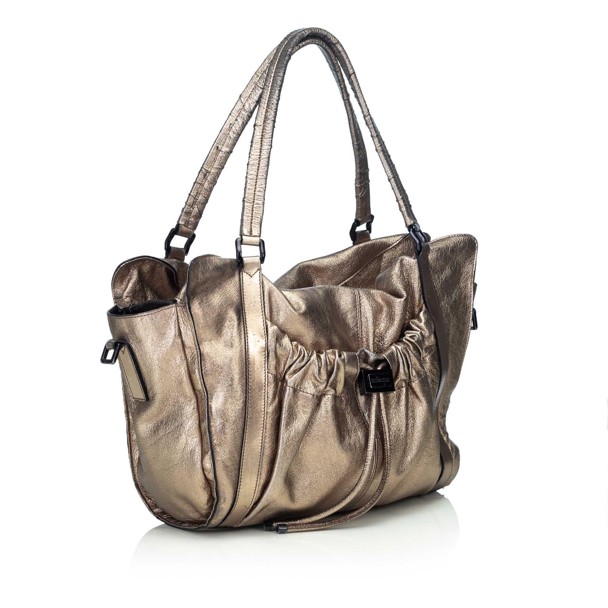 This satchel features a metallic leather body, a front exterior slip pocket with drawstring closure, flat leather strap, a detachable leather strap, a top zip closure, and an interior slip pocket. It carries as B condition rating.

Inclusions: 
This