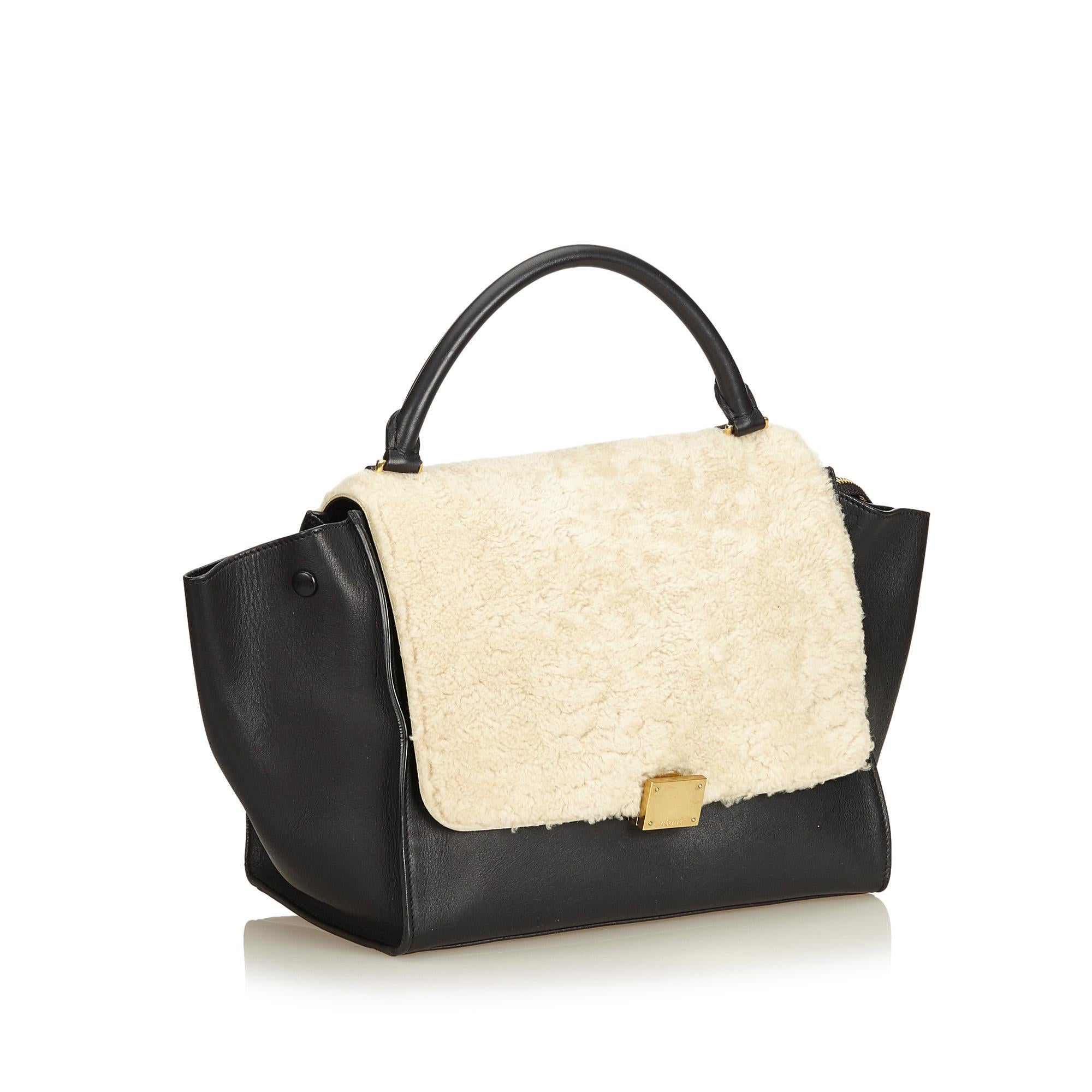 The Trapeze features a leather body with shearling panel at front, single rolled top handle, detachable flat strap, a front flap with a clasp closure, top zip closure, and interior slip pockets. It carries as B+ condition rating.

Inclusions: 
Dust