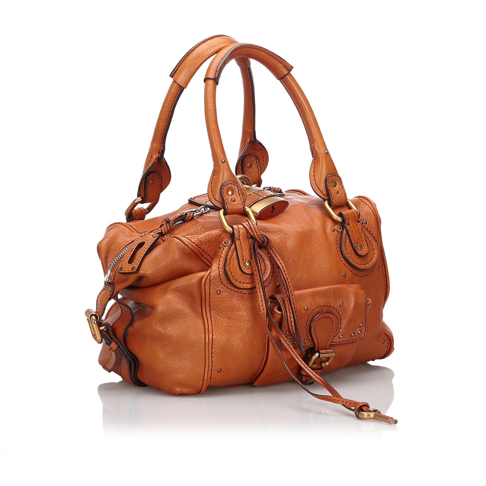 The Paddington features a leather body, rolled straps, an exterior flap pocket, gold-tone hardware, a top zip closure, and an interior zip pocket. It carries as B+ condition rating.

Inclusions: 
Dust Bag
Padlock
Key
Dimensions:
Length: 24.00