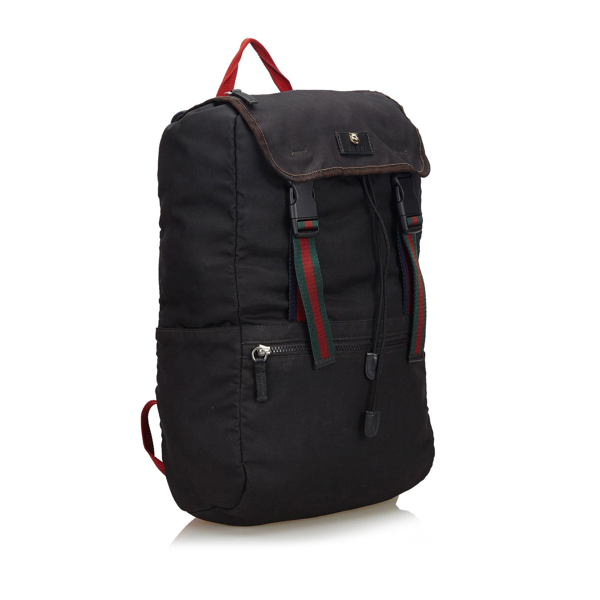 This backpack features a canvas body, a flat top handle, a flat adjustable shoulder strap, a top flap with buckle closures, a drawstring closure, exterior zip and slip pockets, and an interior zip pocket. It carries as B condition
