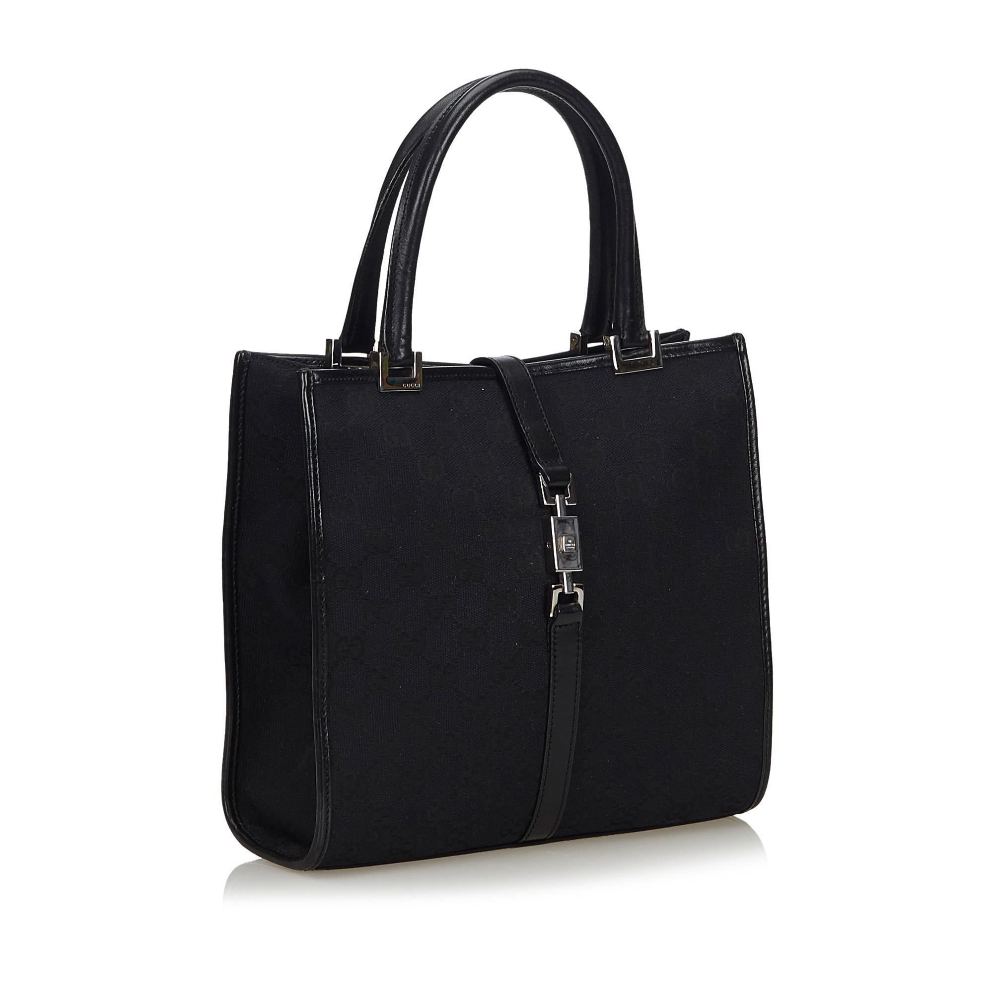 The Jackie tote bag features a canvas body with leather trim, rolled leather handles, a top strap with a metal closure, an open top, and an interior zip pocket. It carries as B+ condition rating.

Inclusions: 
Dust Bag

Dimensions:
Length: 22.00
