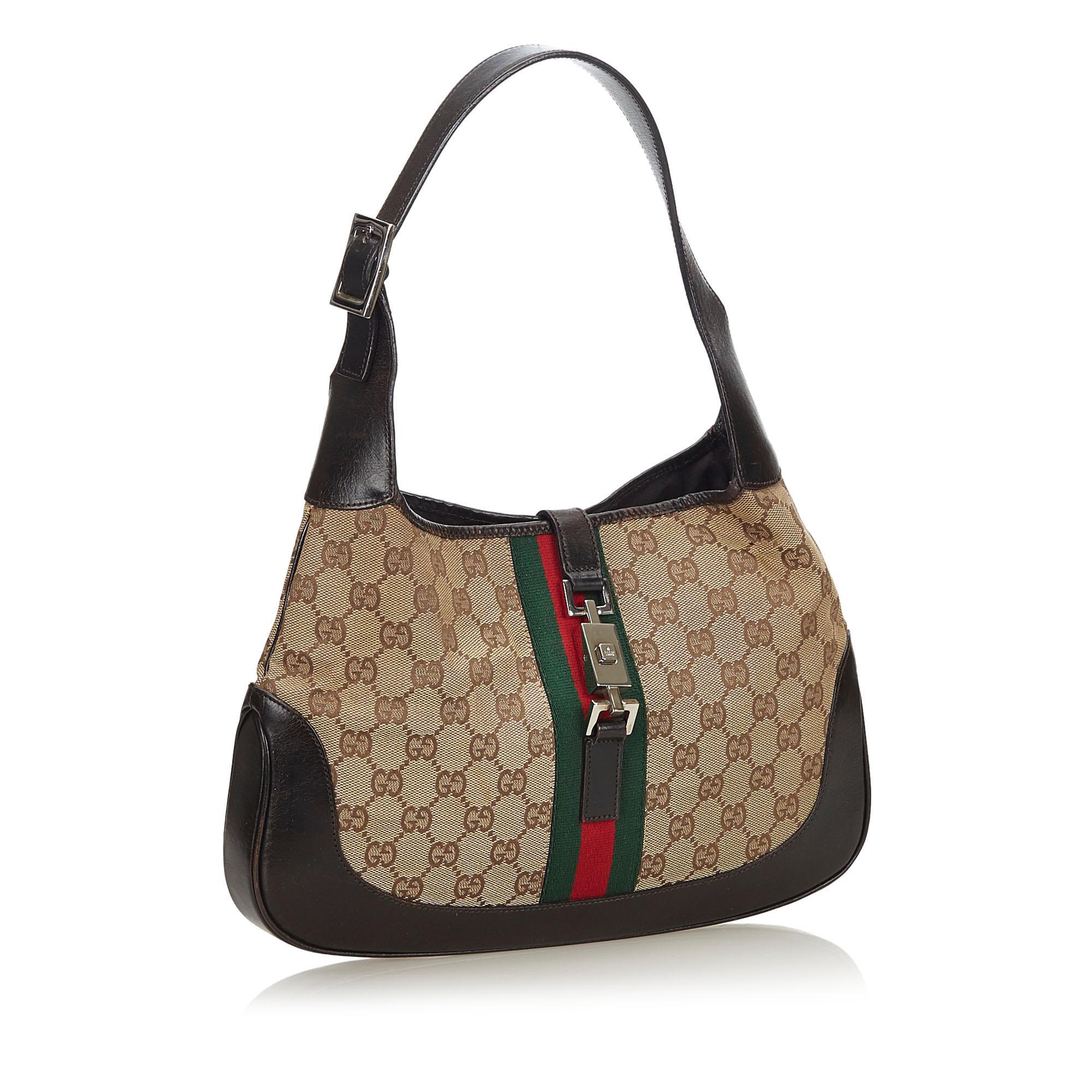 The Jackie features a canvas body with leather trim, a flat leather strap, an open top with a flat strap and a push lock closure, and an interior zip pocket. It carries as B condition rating.

Inclusions: 
Dust Bag
Dimensions:
Length: 21.00