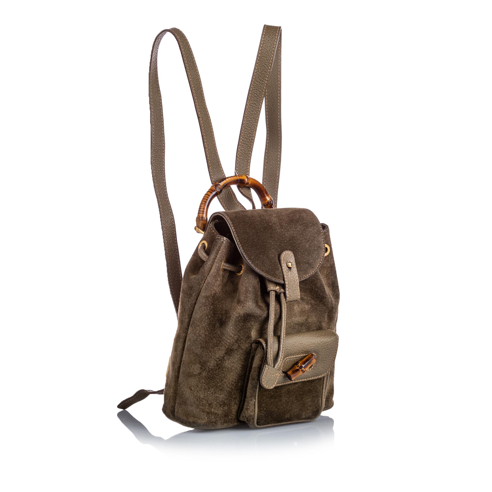 This backpack features a suede body, an exterior flap pocket with a bamboo twist lock closure, flat leather back straps, a bamboo top handle, a top flap with button closure, a drawstring closure, and an interior zip pocket. It carries as B condition