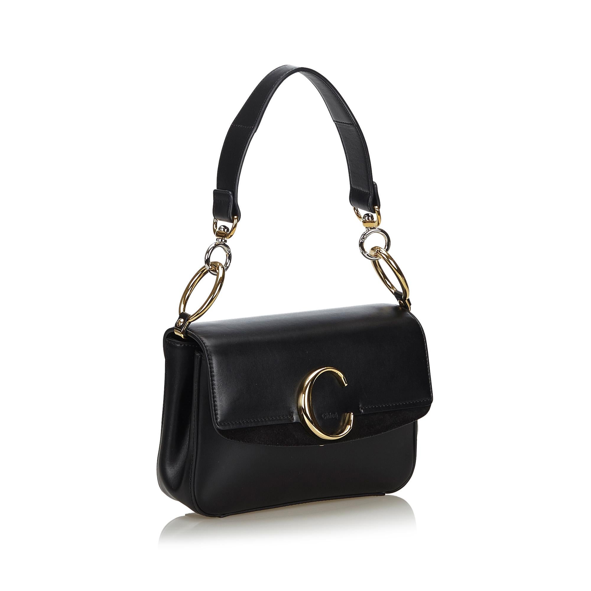 The C Double Carry baguette features a leather body, a back exterior slip pocket, a flat leather strap with gold-tone chain details, a detachable flat leather strap, a front flap with a magnetic closure, and an interior zip pocket. It carries as AB