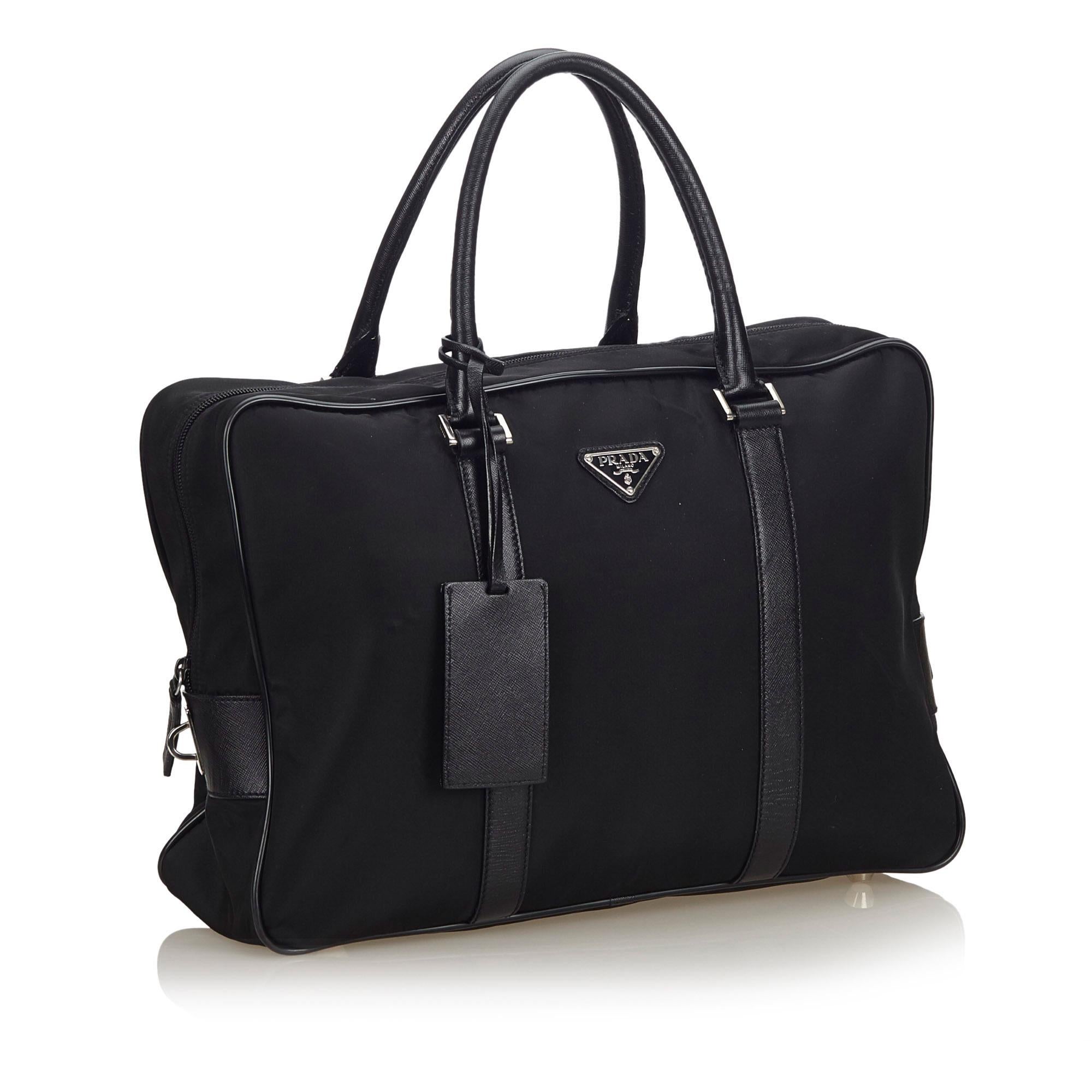 This business bag features a nylon body with leather trim, rolled leather handles, a luggage tag, a top zip closure, and an interior zip pocket. It carries as B+ condition rating.

Inclusions: 
This item does not come with