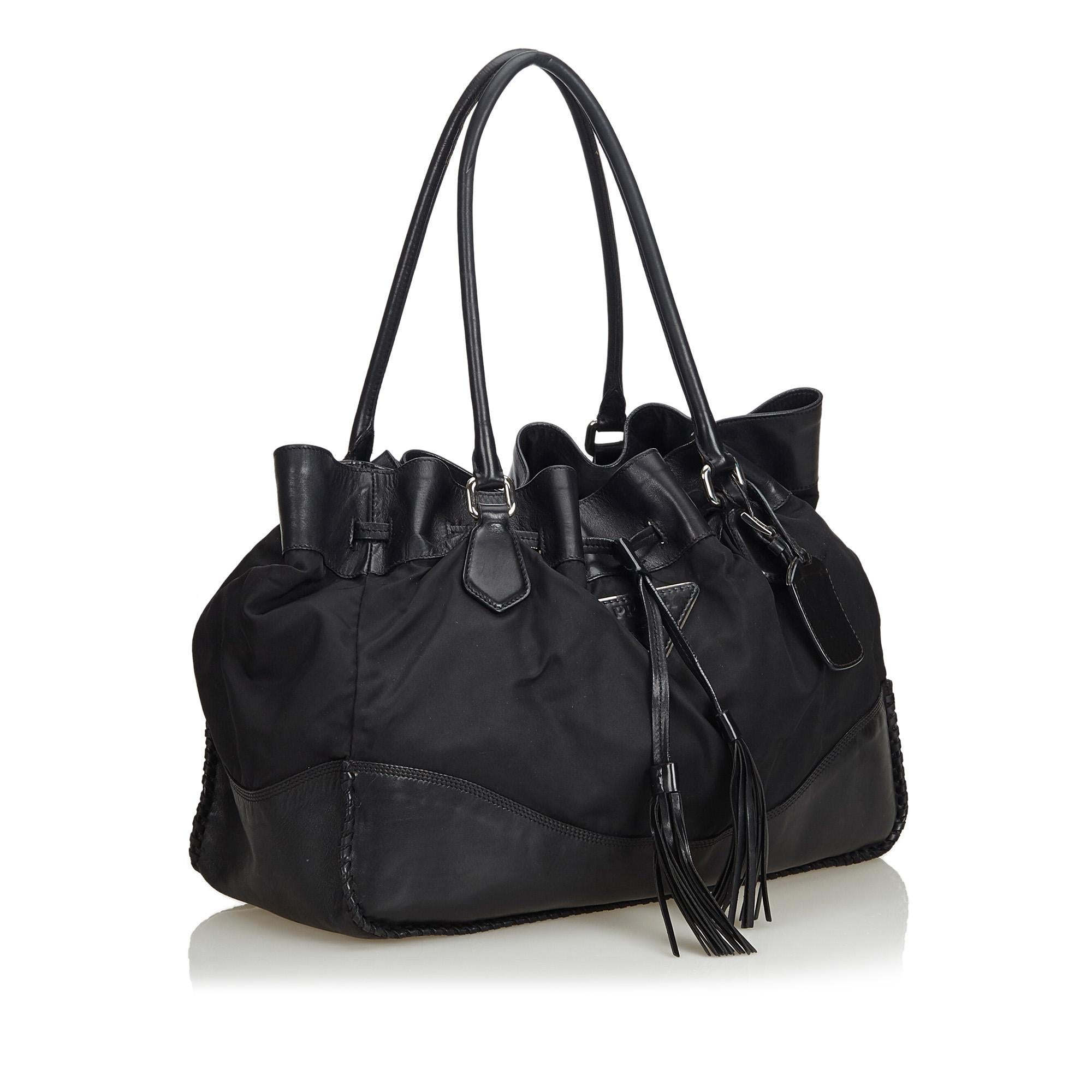 This tote bag features a nylon and leather body, rolled leather handles, a top drawstring closure with tassel detail, and interior zip and slip pockets. It carries as B condition rating.

Inclusions: 
This item does not come with