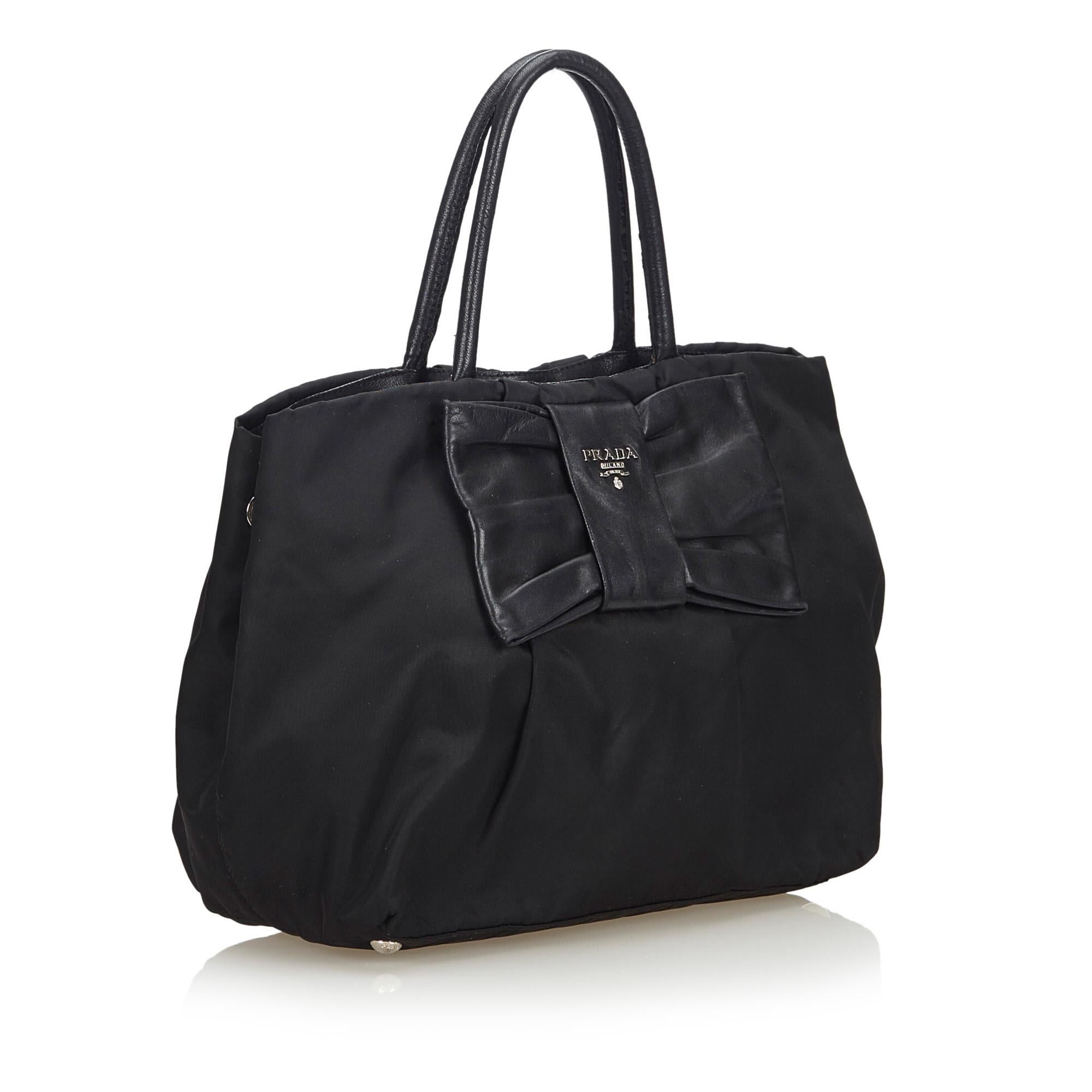 This handbag features a nylon body with a leather ribbon detail, rolled leather handles, an open top with a magnetic snap button closure, and an interior zip pocket. It carries as B+ condition rating.

Inclusions: 
This item does not come with