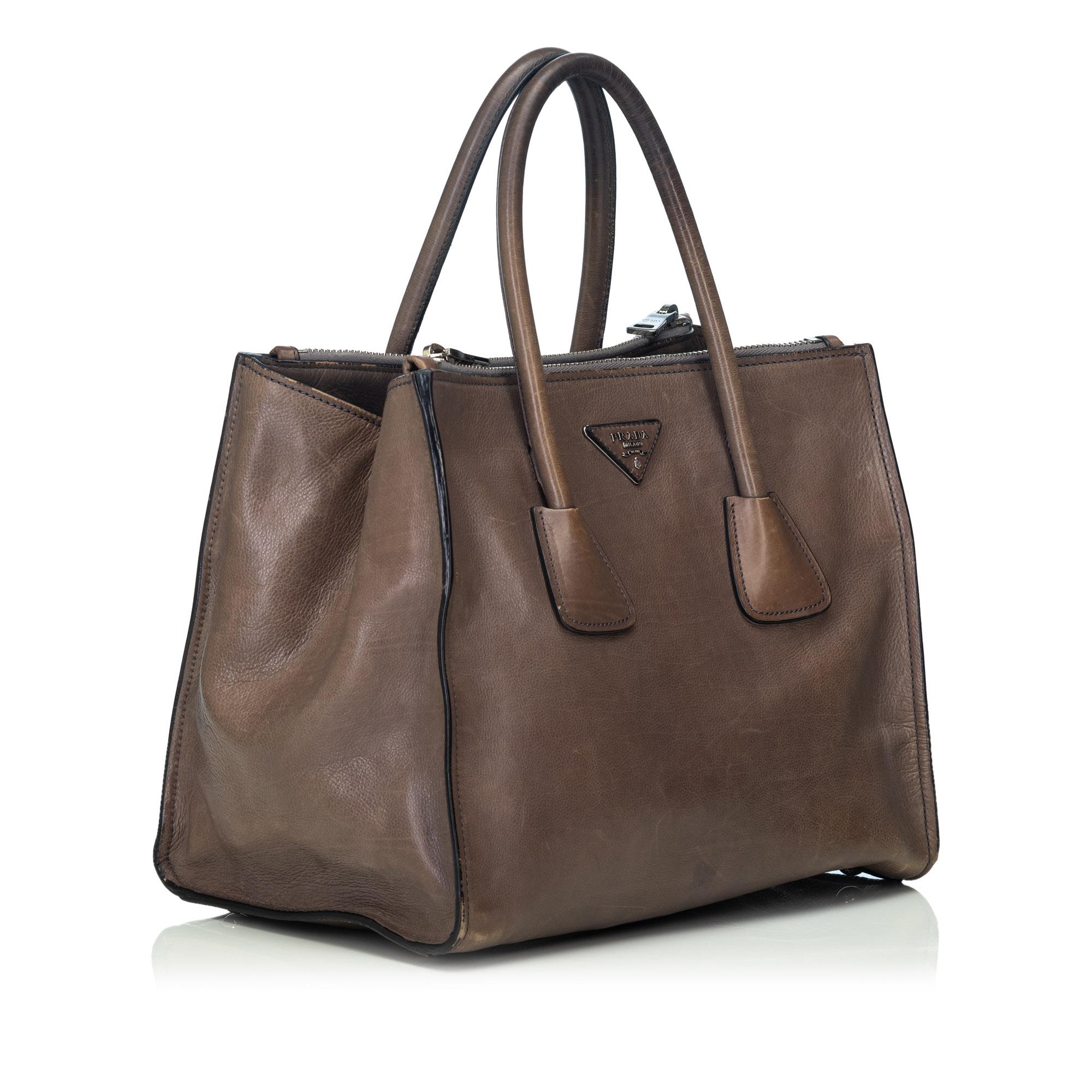 The Twin satchel features a calf leather body, rolled leather handles, a detachable flat leather strap, an open top with magnetic snap button closure, top interior zip compartments, and interior zip pockets. It carries as B condition