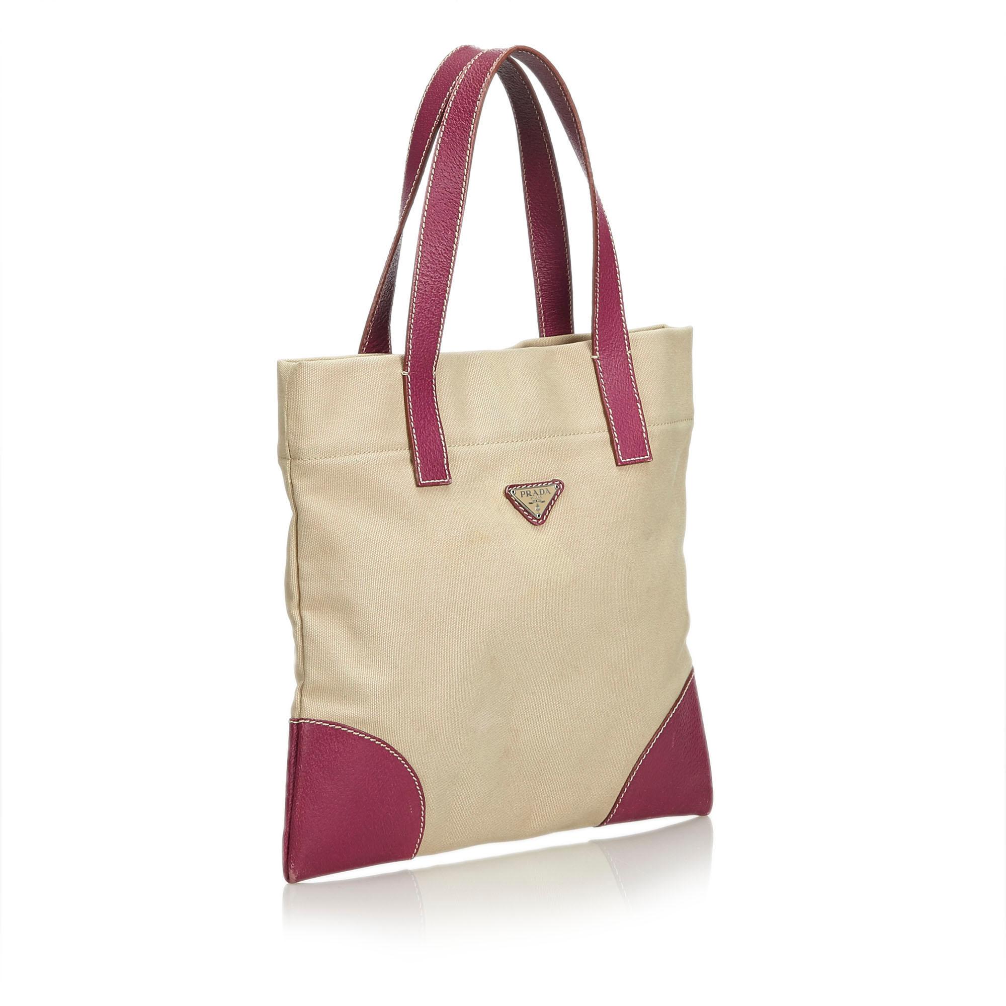 This tote bag features a canvas body with leather trim, flat leather straps, an open top with a magnetic snap button closure, and an interior zip pocket. It carries as B condition rating.

Inclusions: 
This item does not come with