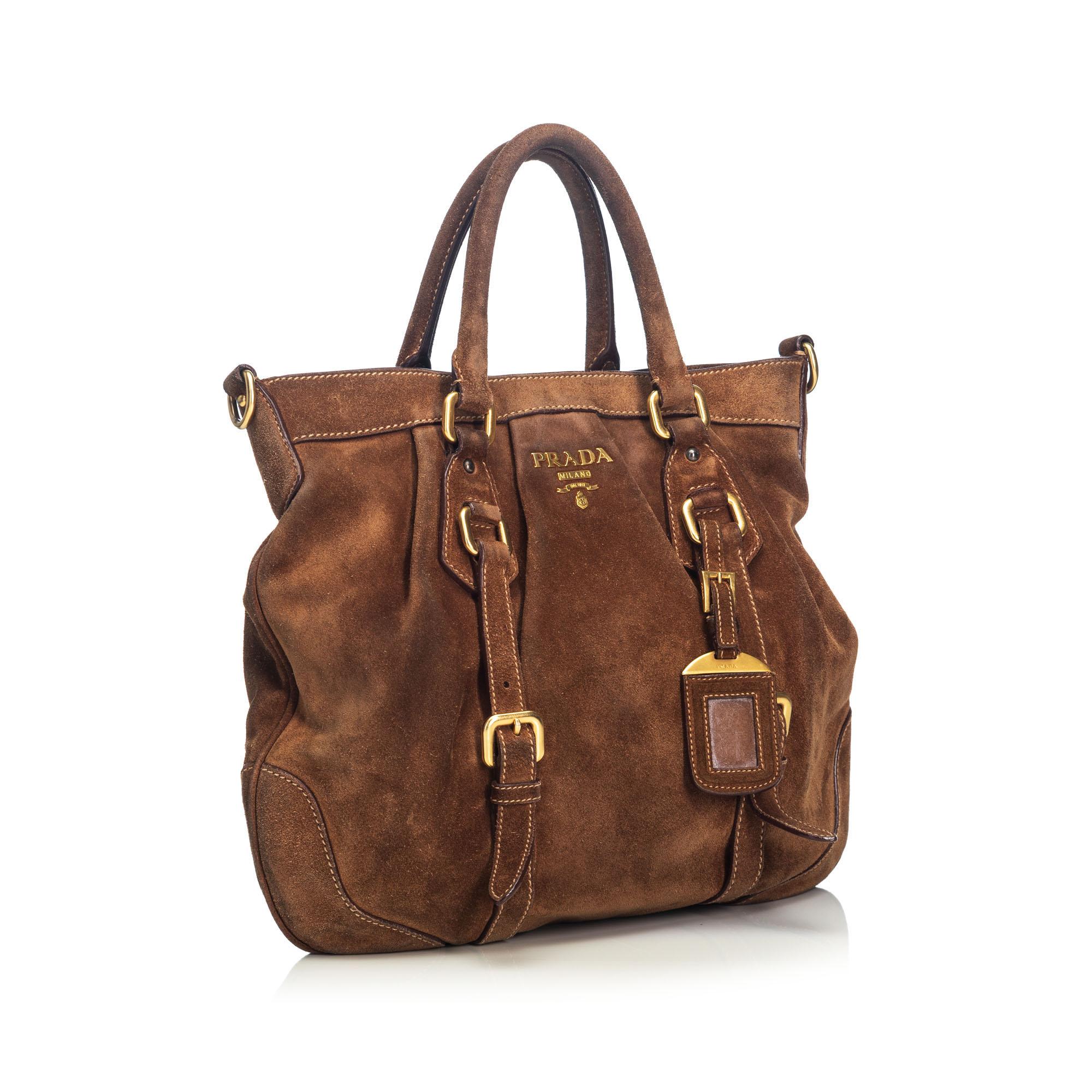 This satchel features a suede body with leather trim, rolled leather handles, a detachable flat strap, an open top with a magnetic snap button closure, and interior pockets. It carries as B condition rating.

Inclusions: 
Dust