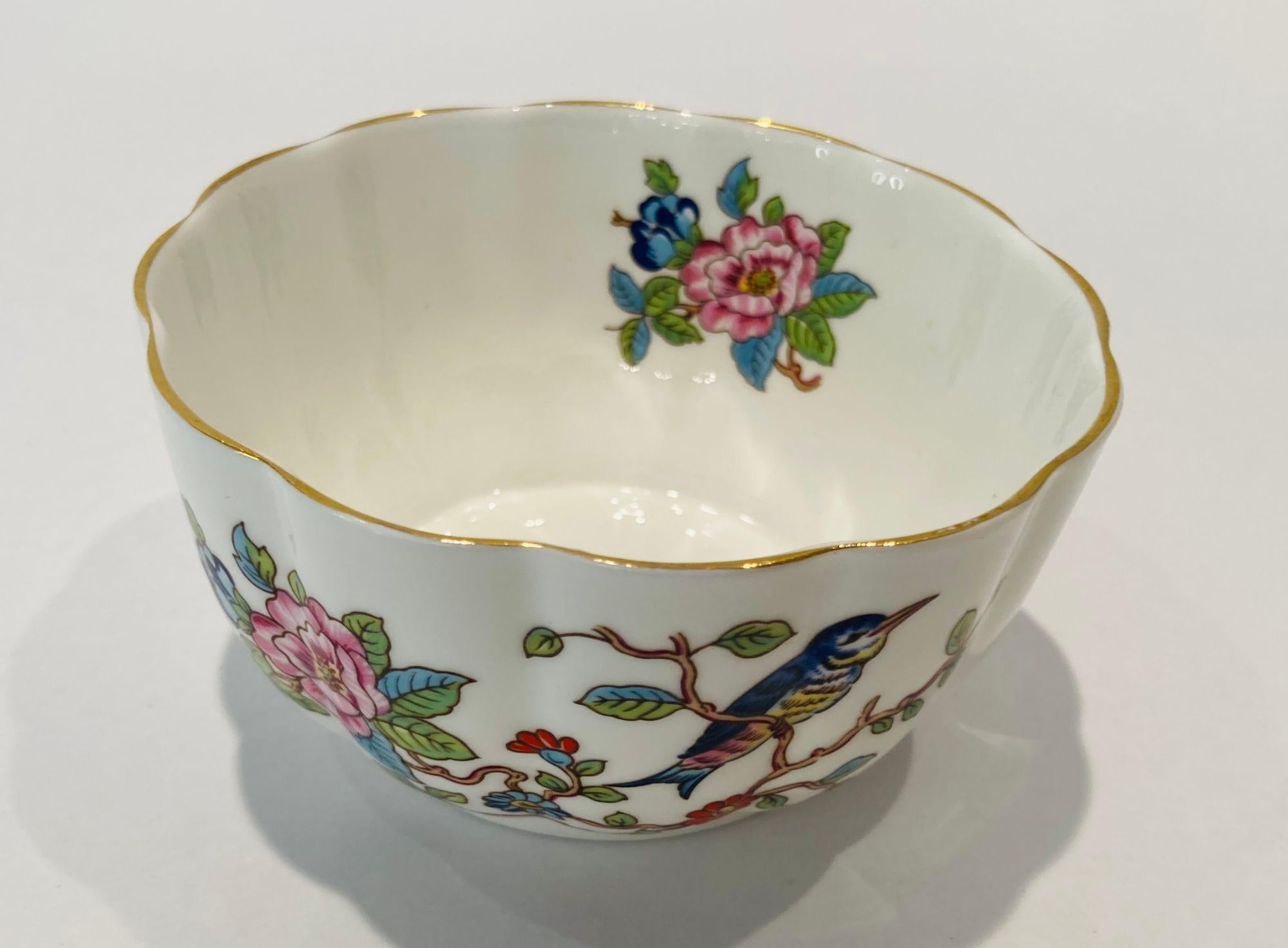 Bol Aynsley en porcelaine de Chine finement dessiné avec le motif Pembroke et une bordure dorée, avec un oiseau bleu cobalt brillant perché sur une branche d'un côté et une gerbe de fleurs de l'autre côté.
La société Aynsley Fine English China