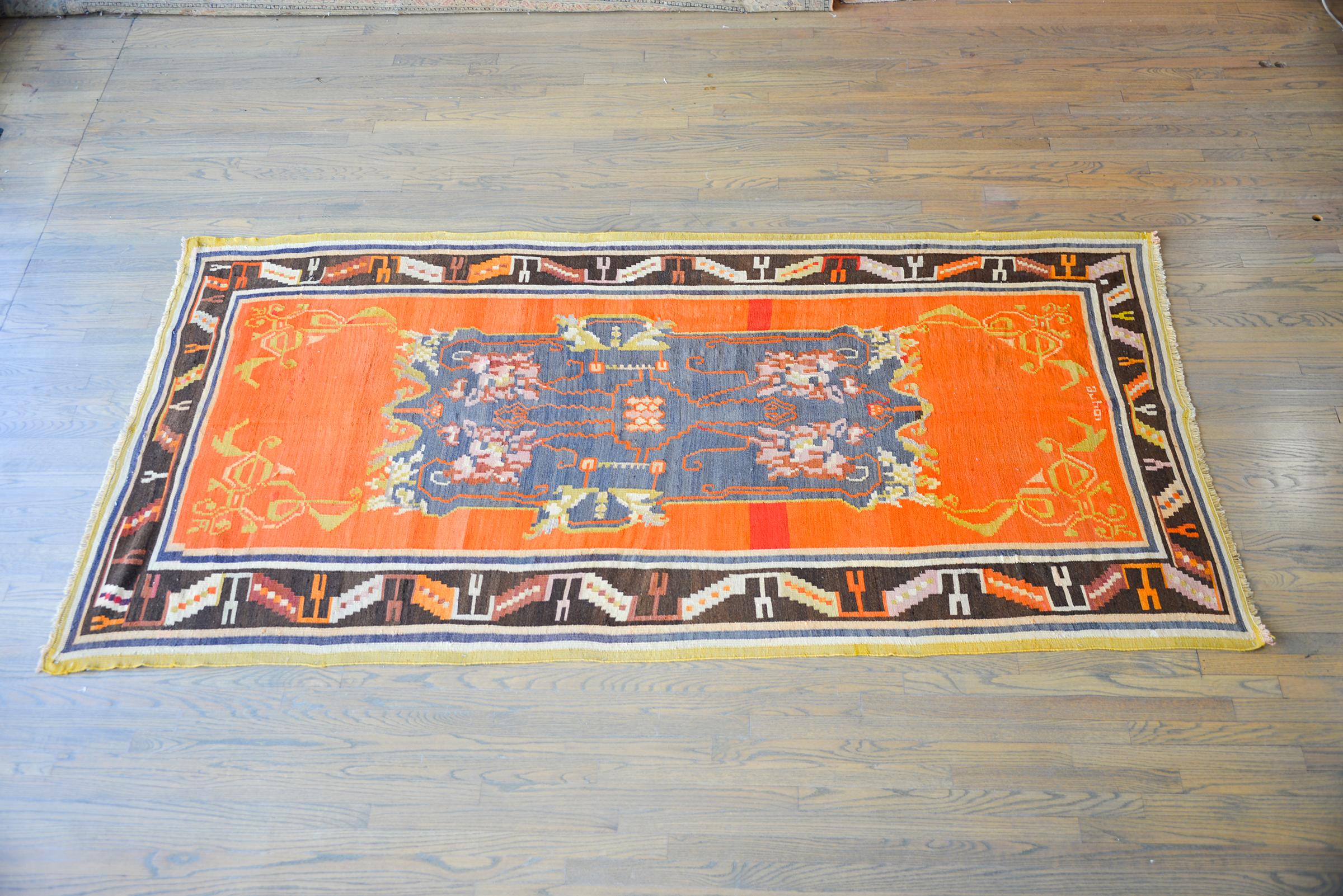 A gorgeous vintage Afghani Azari kilim with a boldly woven pattern with stylized flowers and scrolling vines, all woven in pinks, golds, reds, and black, set against a brilliant orange background. The border is interesting with a geometric stylized