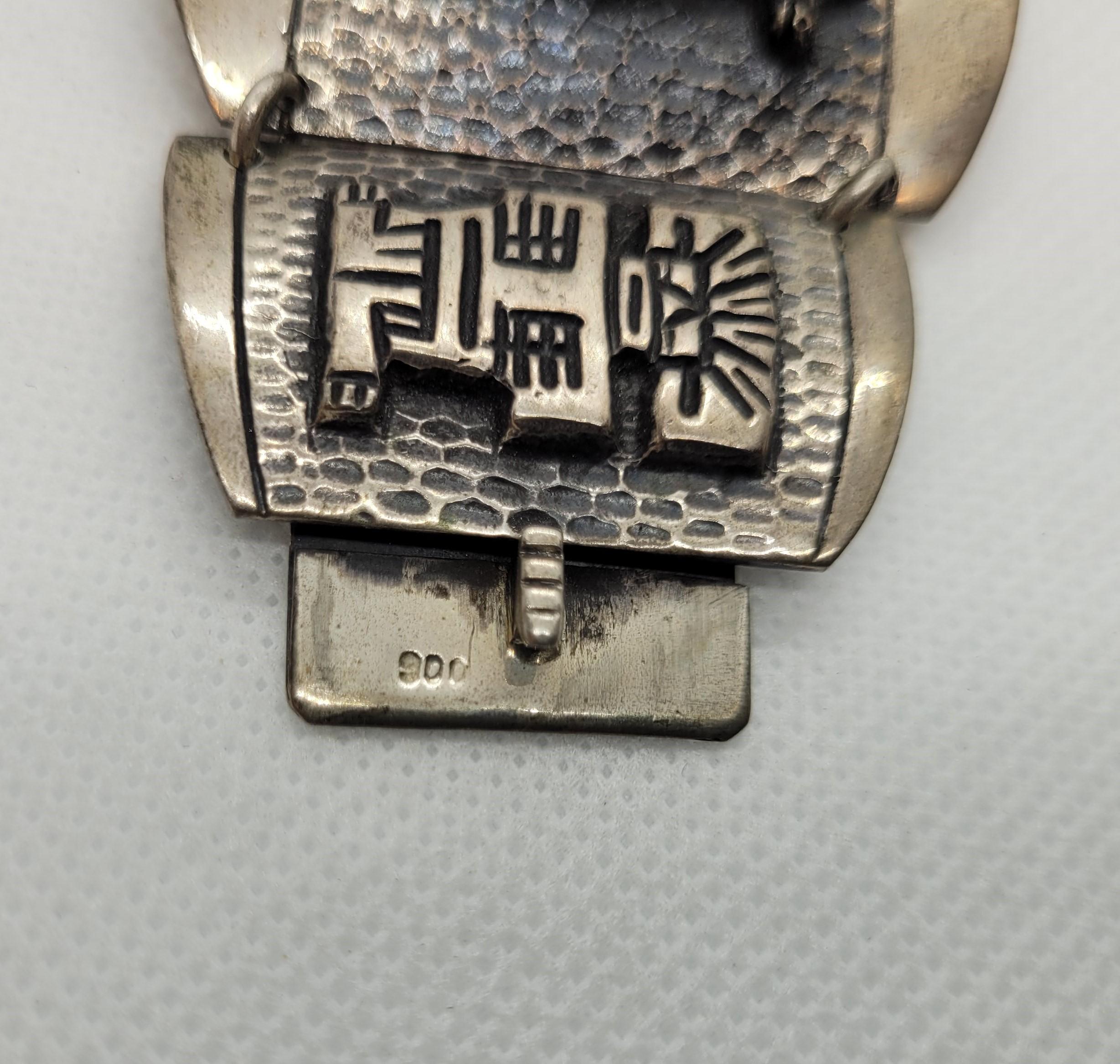 Vintage 900 silver bracelet with an Aztec Mayan design that is 1.75 inches wide, 7.5 inches long, and 70 grams, with a push-in clasp and safety chain. The design symbolizes a llama, warrior, and masked Aztec. Overall, this bracelet is in very good