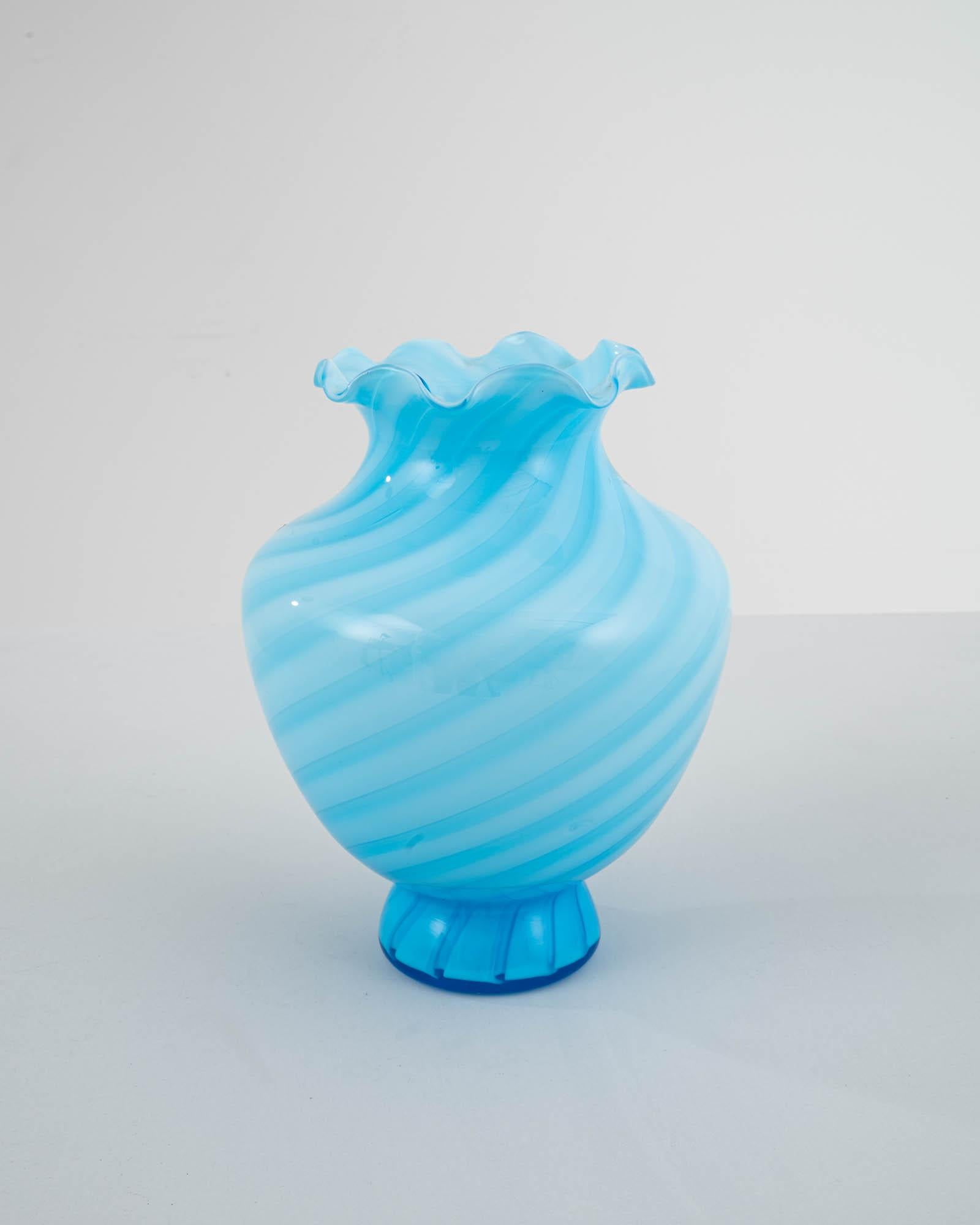 A beautifully crafted glass vase tinted in a light blue shade with a small metallic sticker indicating the maker. Both a decoration by itself or a vase for a bouquet, this piece comes from twentieth Century Italy, where glass working —both as