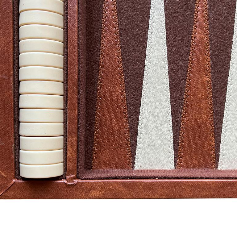 A vintage backgammon set in a carrying case. This set includes brown and white game pieces and dice and is in a faux leather carrying case. This is a complete set. The carrying case is in faux brown leather, with white stripes down the middle on the