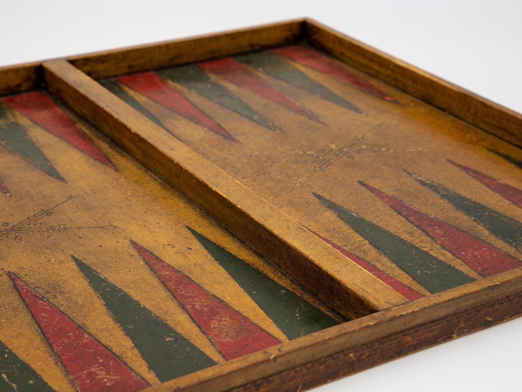 An early 20th century Backgammon game box. The interior is made of cognac, green, and red dyed leather. The exterior is embossed with a gold vine border. Wear consistent with age and use.
