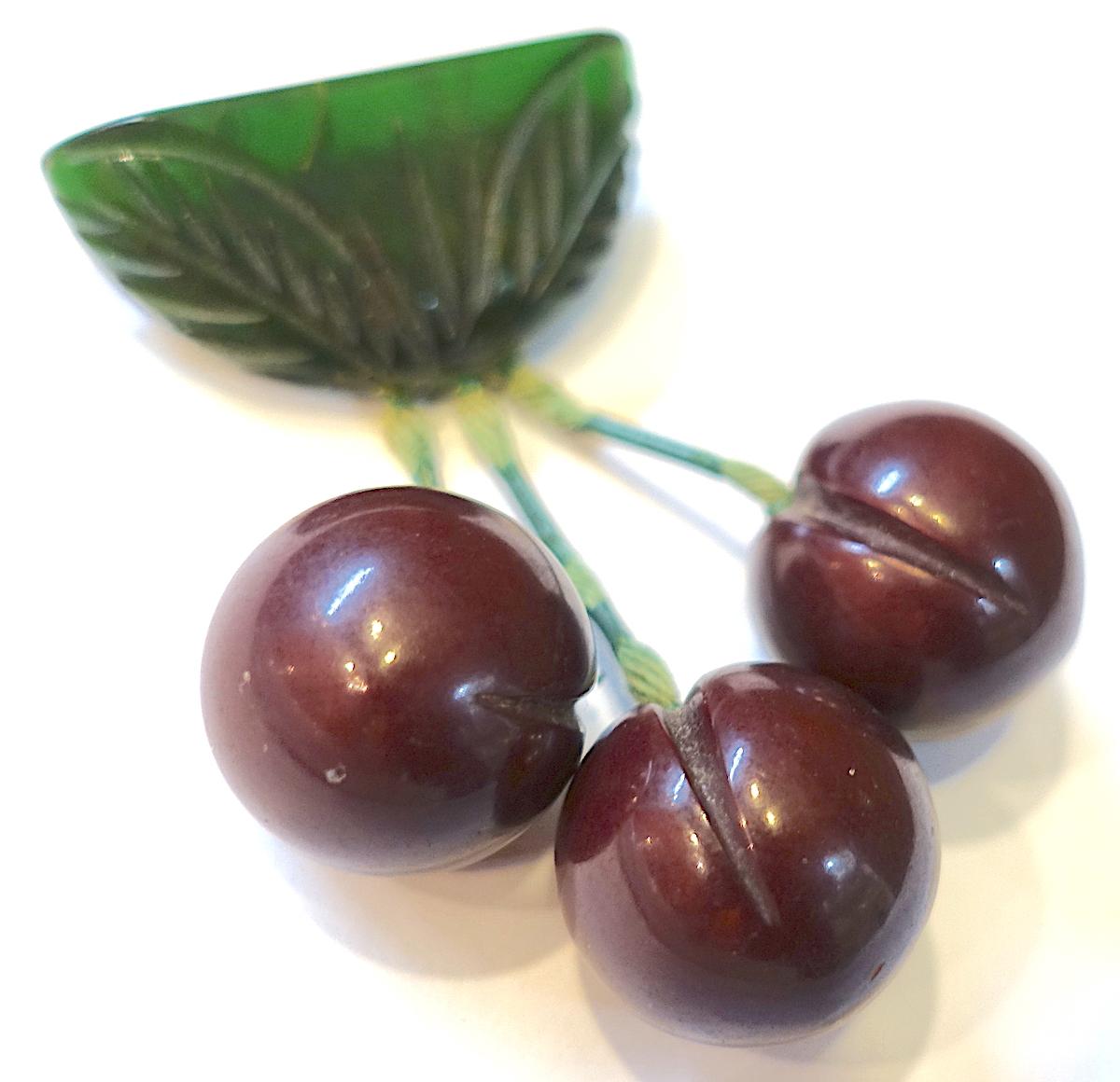 This Bakelite brooch features dark purple colored cherries suspended from green carved leaves on top.  In excellent condition, this brooch measures 2-1/4” x 1-1/4” with a c-pin clasp.