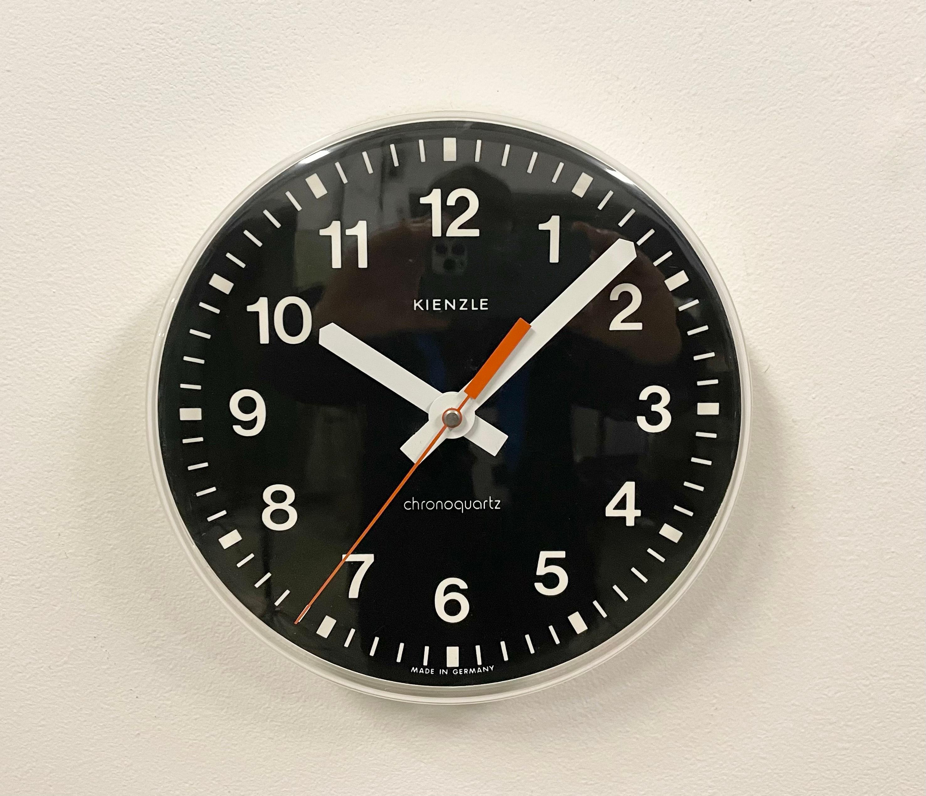 Vintage wall clock was produced by Kinzle Clock in Germany during the 1970s. It features a white bakelite frame with black dial and a clear plastic glass cover. The battery-powered clockwork requires one C battery. The diameter of the clock is 22