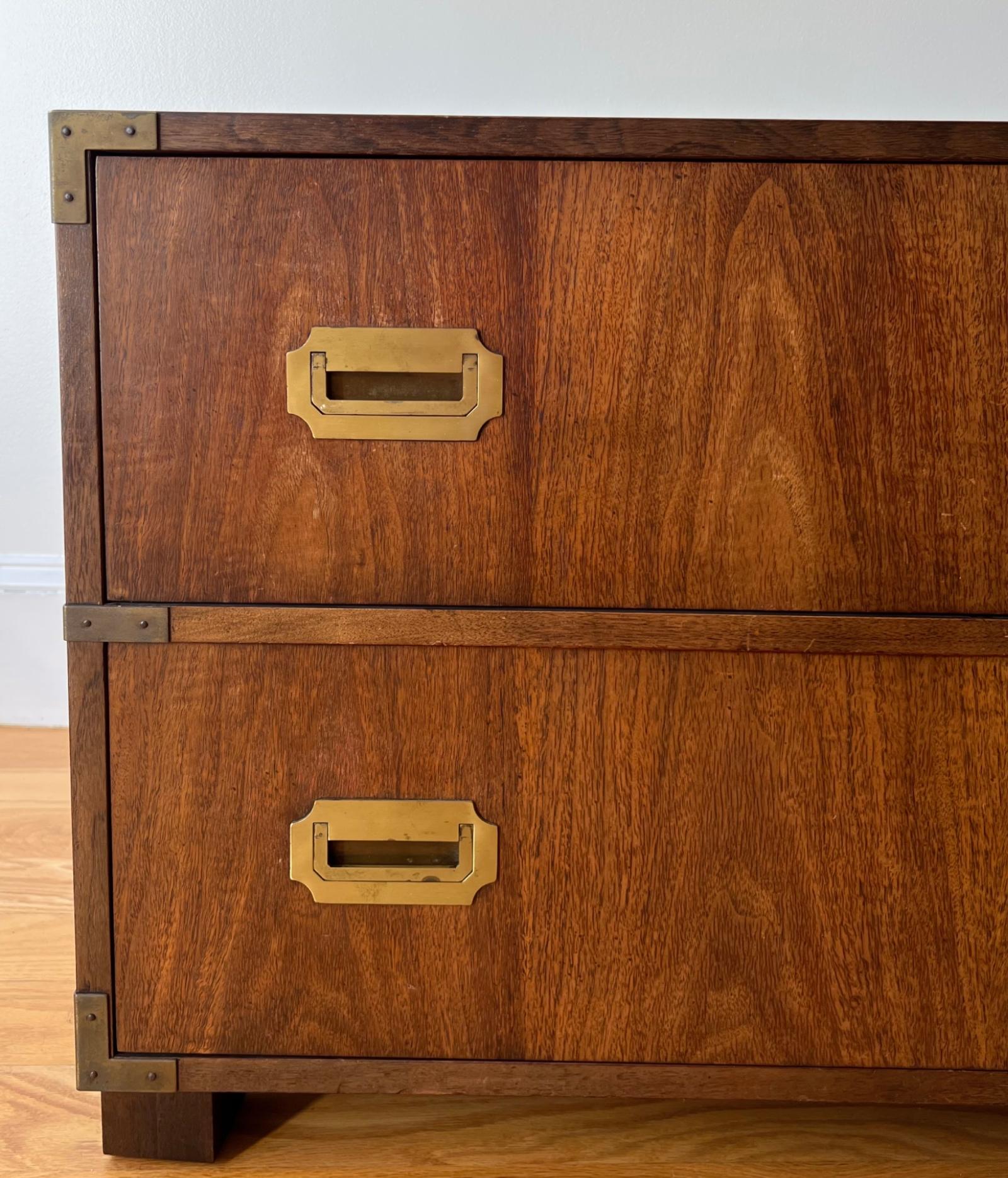 Une commode classique à deux tiroirs de style campagne par Baker Furniture, fabriquée en placage de noyer avec des façades de tiroirs assorties et accentuées par des poignées encastrées en laiton affleurant et des supports d'angle. 

Signé avec une