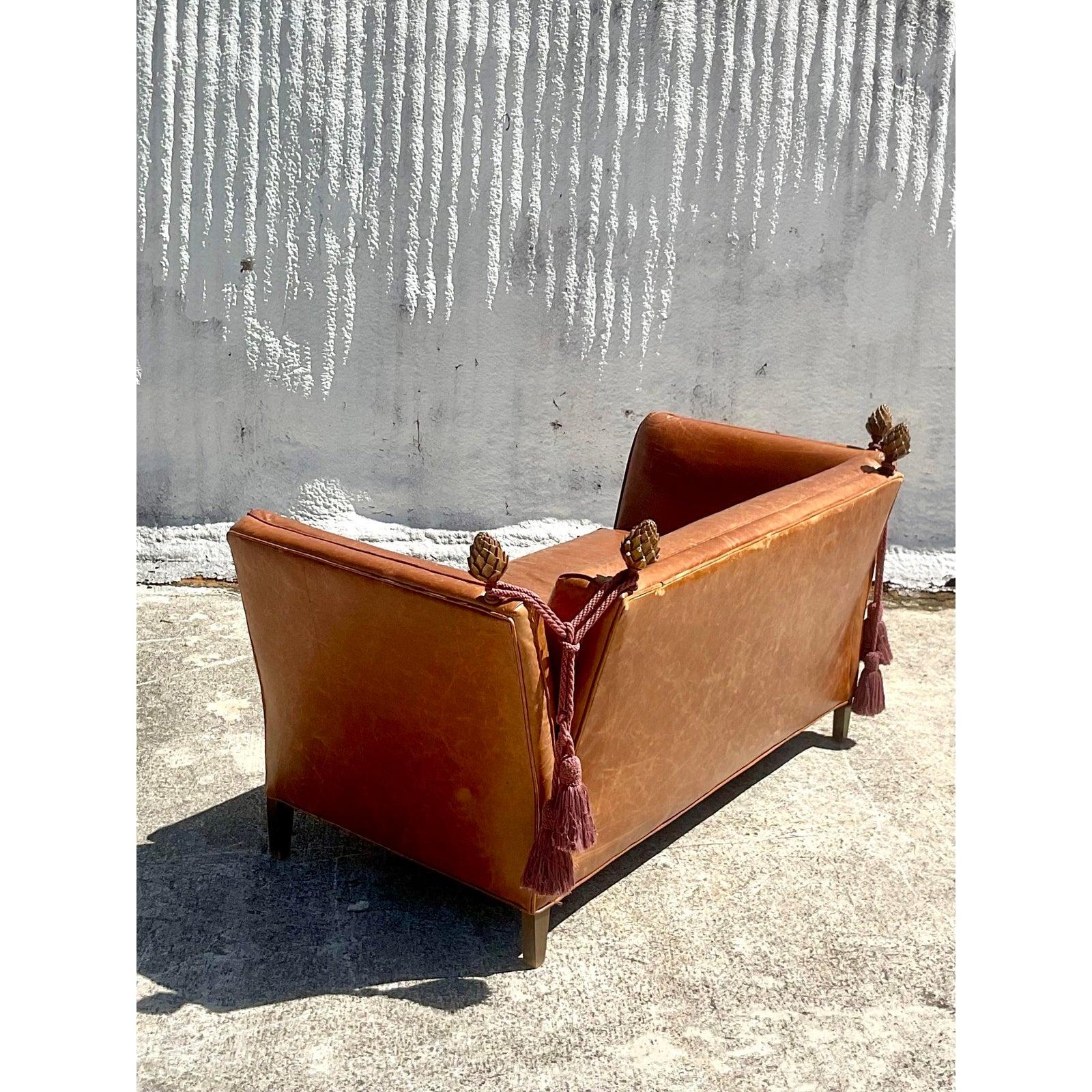 Incredible vintage Baker Knole loveseat. Beautiful distressed leather in a rich brown color. Carved artichokes adorn the back wrapped in. Swag cord and tassel. Acquired from a Palm Beach estate.