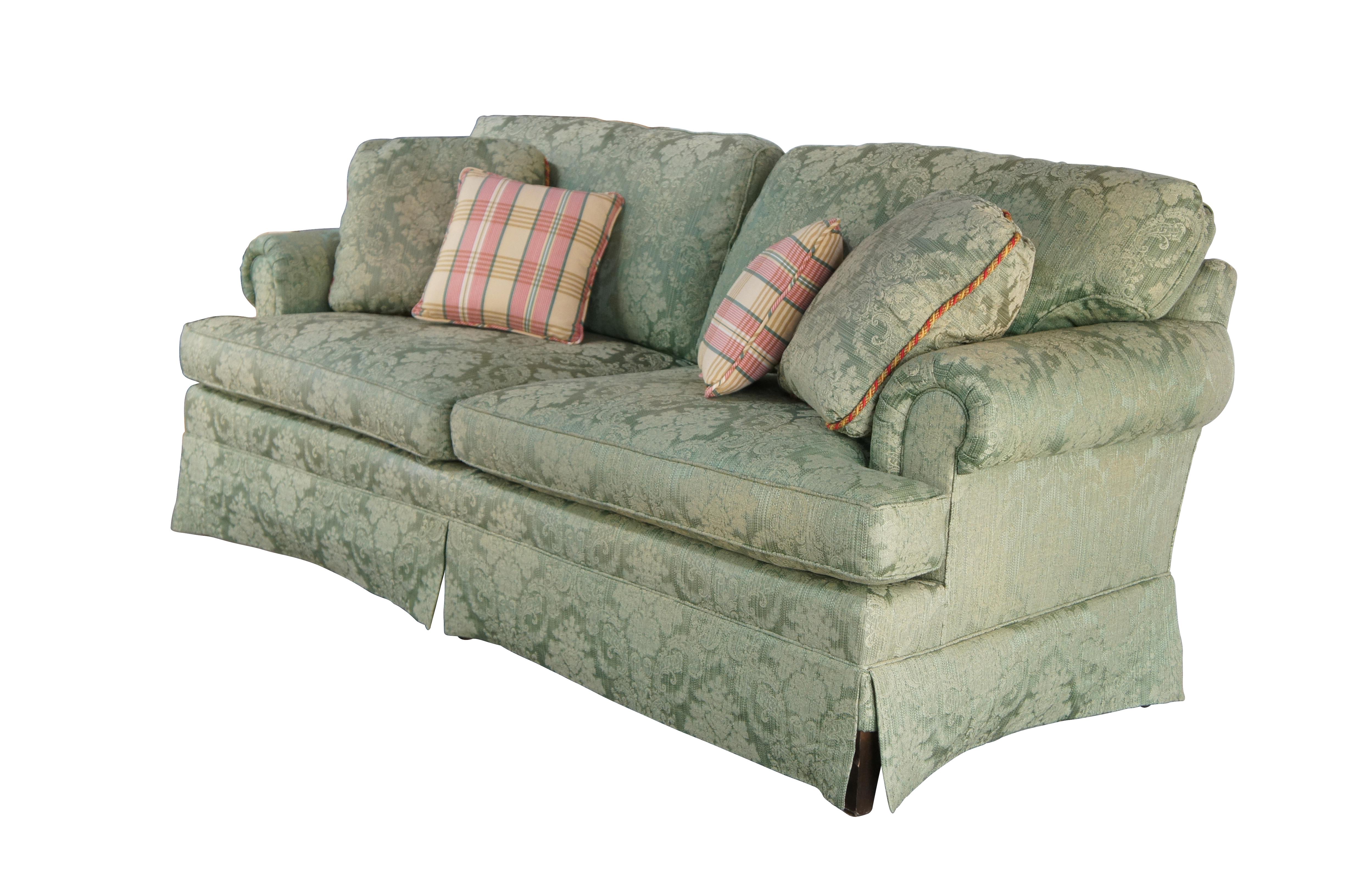 A charming vintage Baker Furniture traditional rolled arm sofa, circa 1995. Features green damask fabric inspired by French design with floral bouquets centered around laurel leaf and acanthus sprays. Includes two matching throw pillows and two