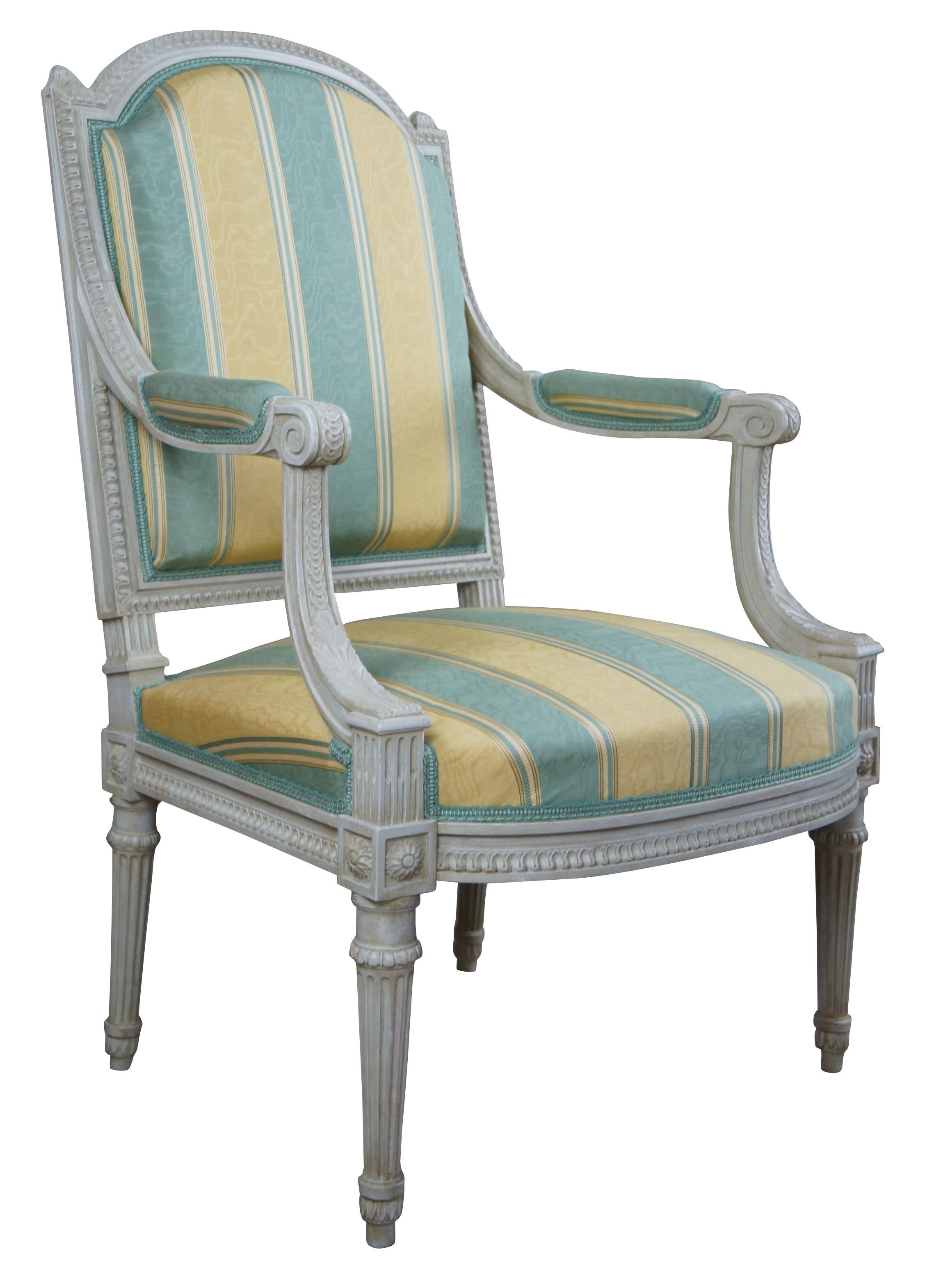 Vintage Baker Furniture Louis XVI / French Provincial Feuteuil armchair featuring tulip and acanthus accents, a domed back with finials, upholstered arms and tapered fluted legs. The chair is upholstered in a green and yellow silk striped fabric