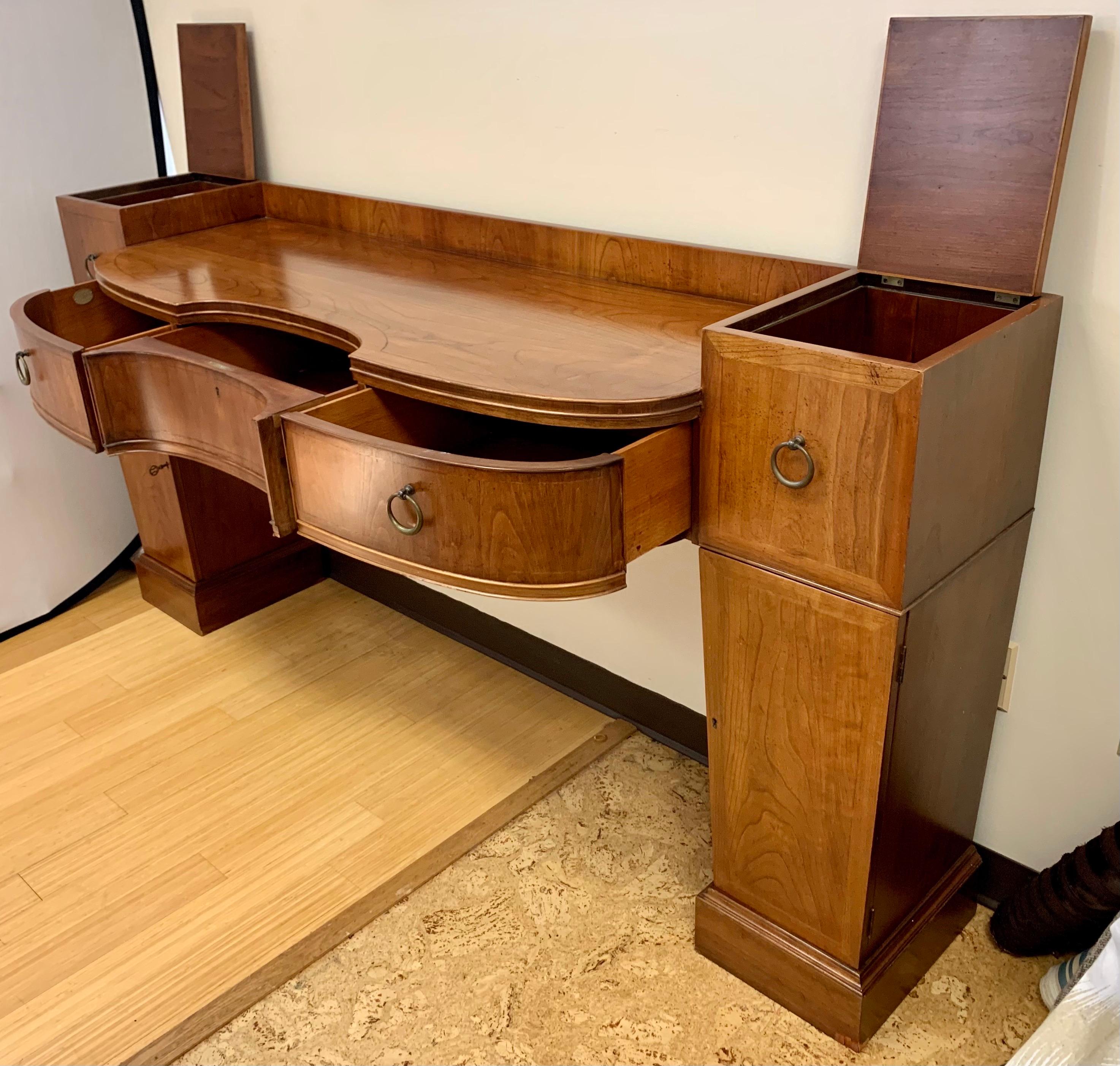 Elegant signed Baker Furniture console credenza featuring a shaped center drawer and side pedestals that flip open for extra storage on top as well as doors that open on bottom with shelves for more storage. Great lines and better scale. Age