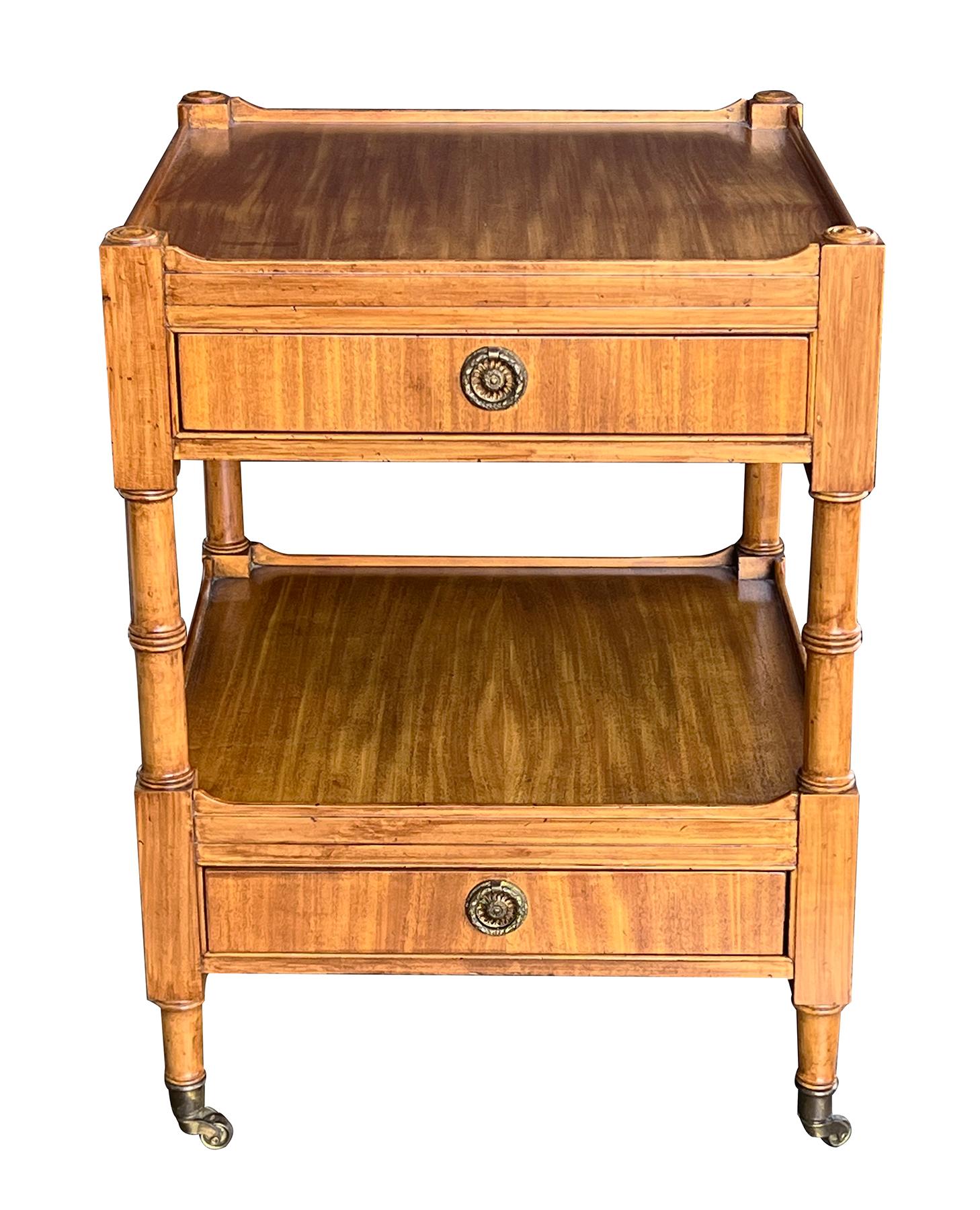 a good quality cabinet in the neoclassical style with inset square top of ribbon mahogany above a single drawer apron raised on turned supports all joined by a lower shelf over a single drawer; raised on brass casters