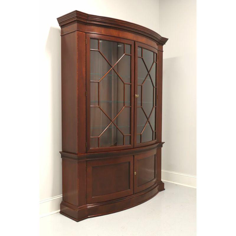 A Traditional style bowfront display cabinet by Baker, from their Historic Charleston collection. Mahogany and mahogany veneers with brass hardware. Upper lighted cabinet features dual lockable bowed glass doors with fretwork revealing six