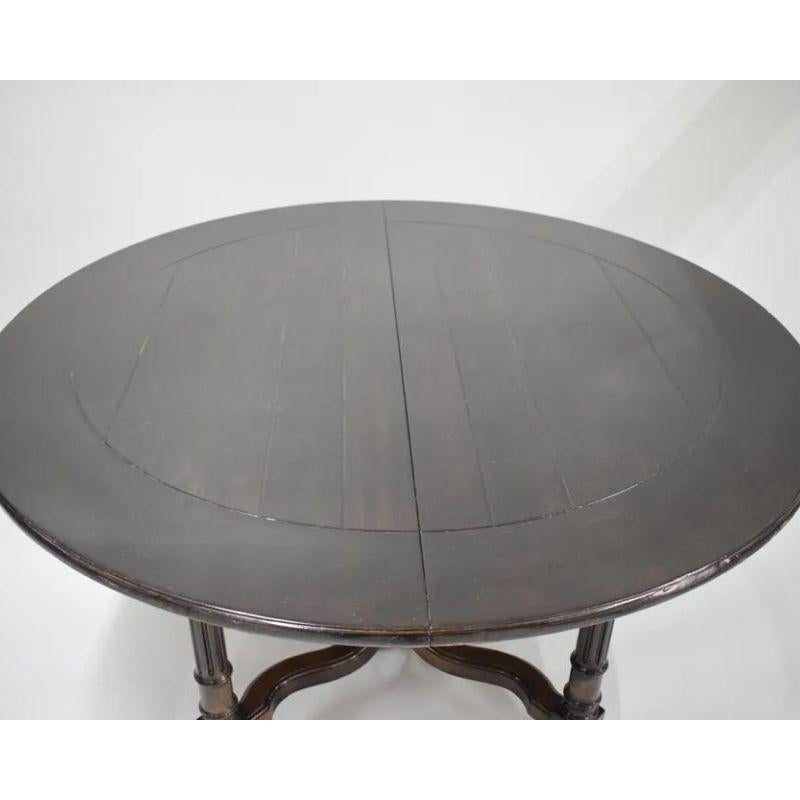 A vintage Baker Milling Road round, dark wood dining table with curved trestle base and carved and reeded legs ending in round feet. Two leaves, each measures 20