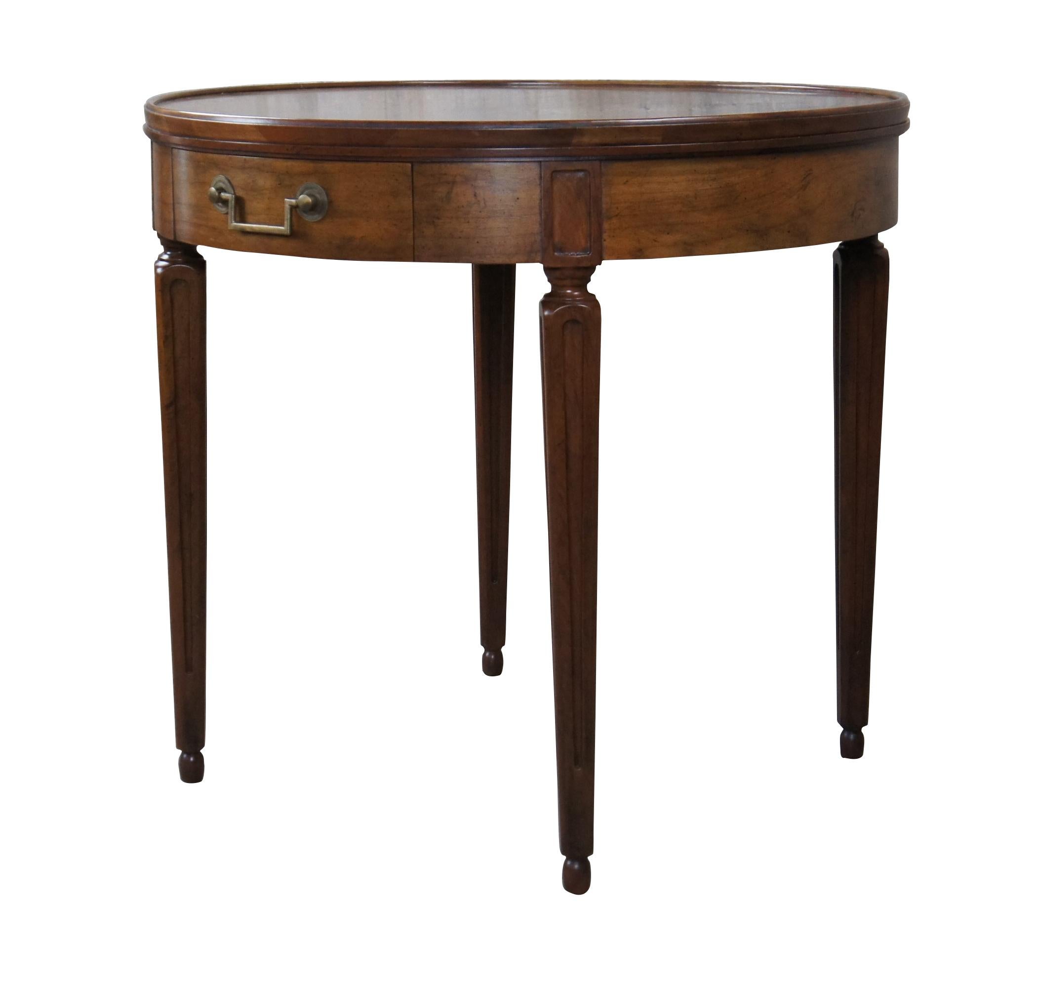 An impressive Baker Furniture Neoclassical inspired side table, circa 1980s. Features a round inset top made from walnut with olive ash burl banding. Includes one dovetailed drawer with brass hardware within the frieze set over square tapered legs