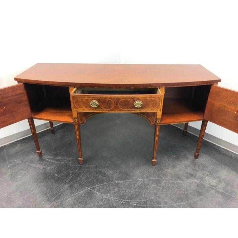 A Hepplewhite style sideboard by Baker Furniture, from their Colonial Williamsburg Collection. Mahogany and satinwood with ample inlay and banding, bowfront, tapered legs and spade feet. Center drawer has felt lined silver storage organizer, flanked