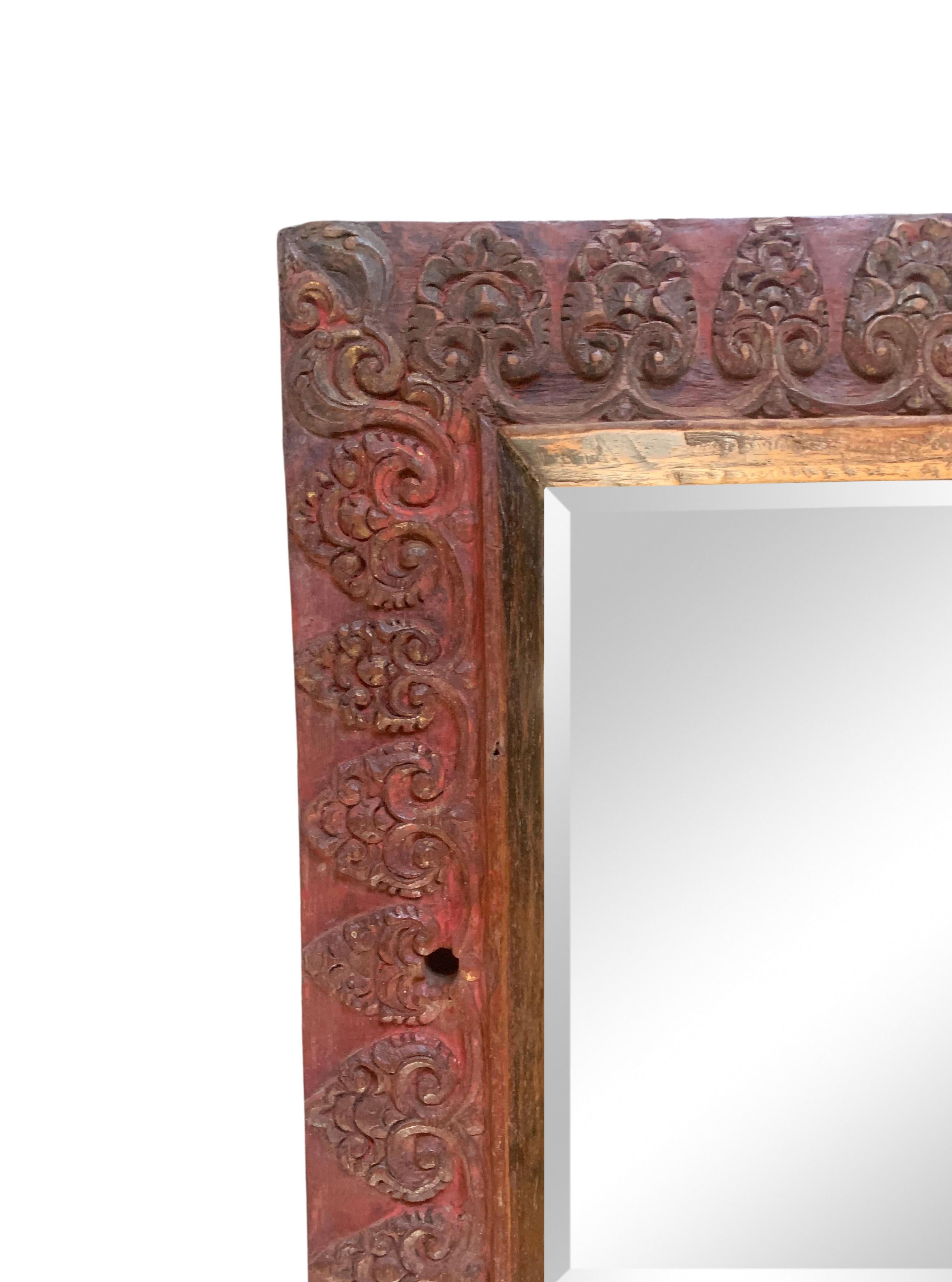 Ce miroir a été fabriqué sur l'île de Bali vers le milieu du 20e siècle et présente de merveilleux détails sculptés balinais et une finition polychrome rouge.